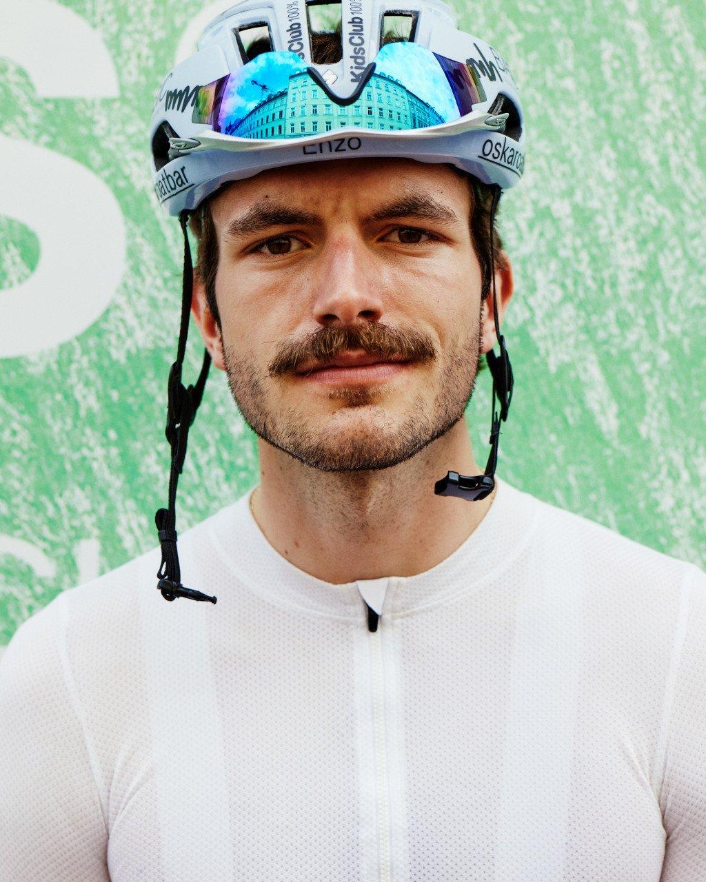 Male cyclist wearing white jersey with cycling helmet against green background