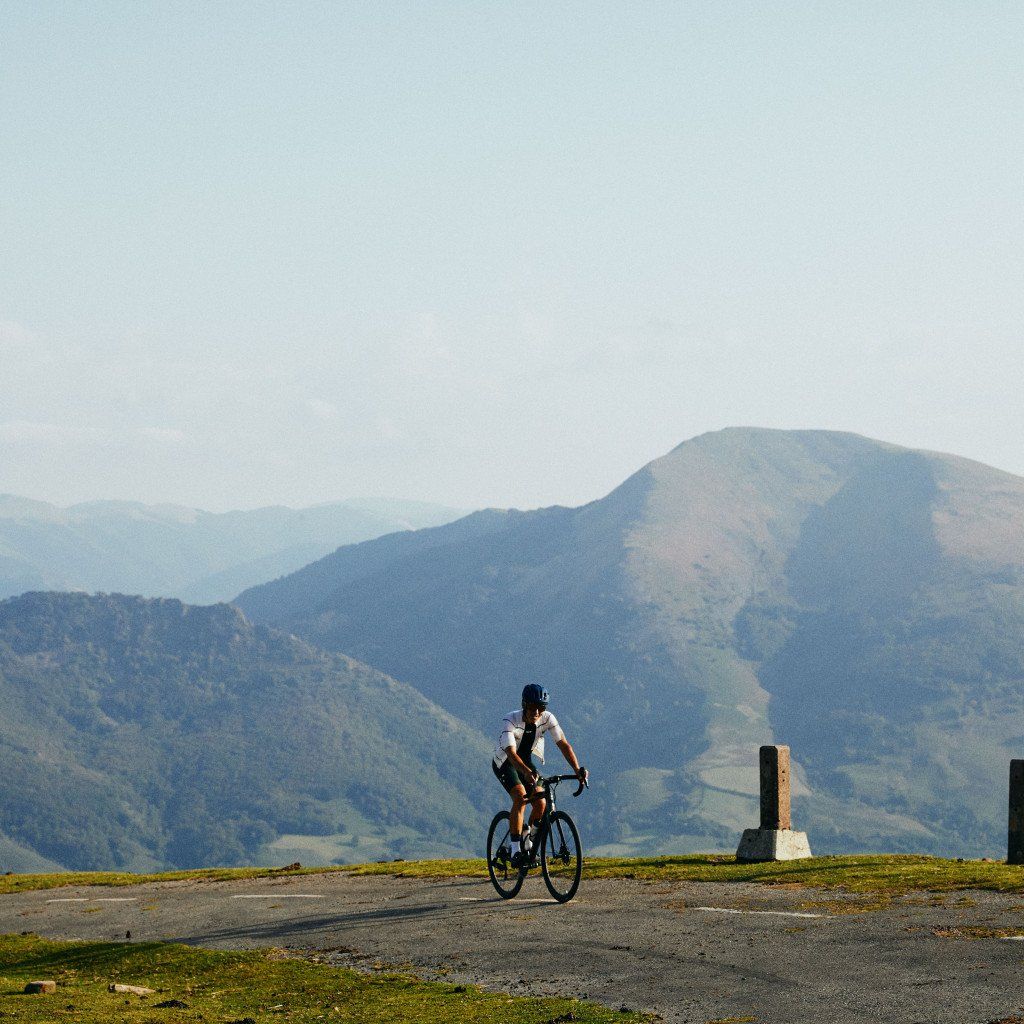 Cyclist in aerodynamic position on mountain road with rolling hills in background