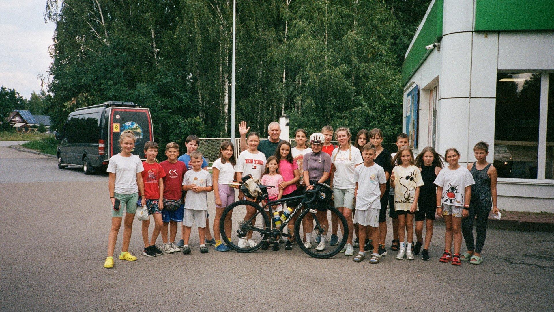 Group photo with cyclist and bicycle surrounded by children and adults outside building