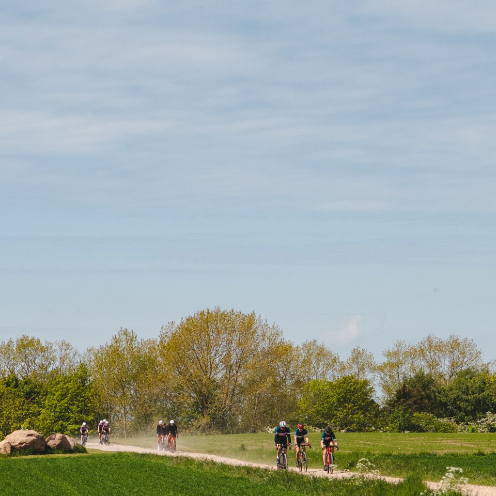 Cyclists riding on gravel path through green countryside under blue sky
