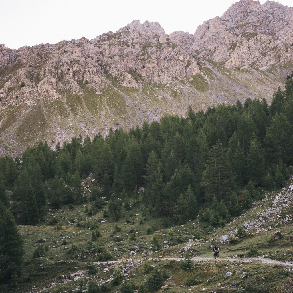 Cyclist riding through alpine mountain landscape with rocky peaks and forest