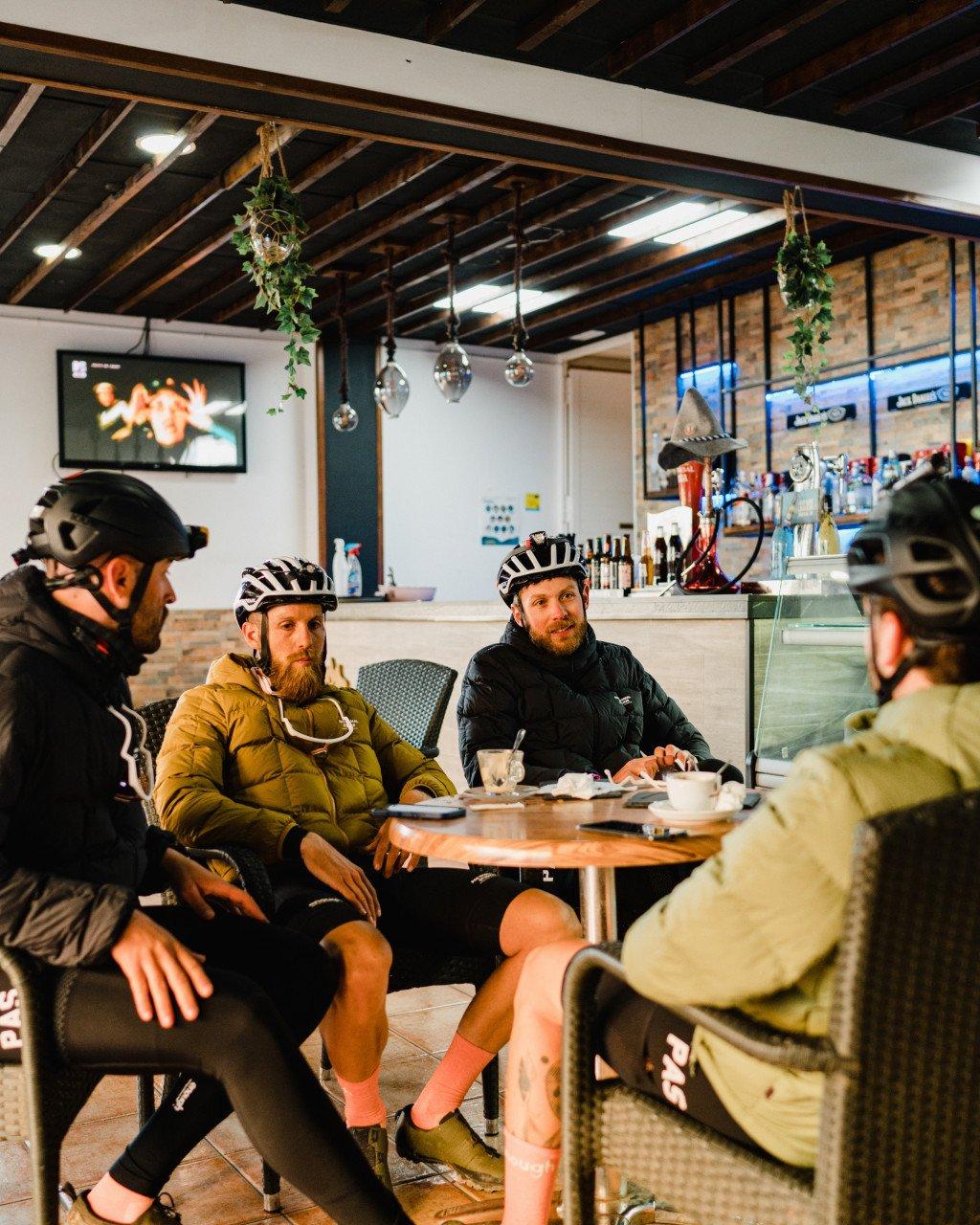 Cyclists in winter jackets and helmets relaxing at cafe table with coffee after ride