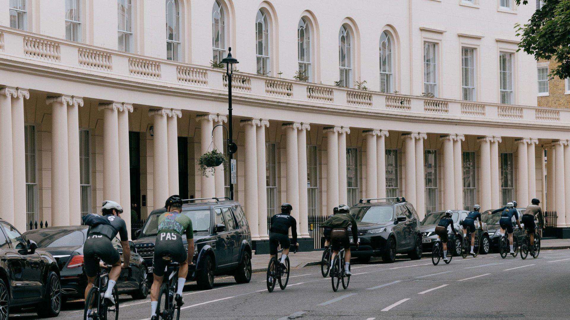 Cyclists in dark green jerseys riding through London street with classical white columned buildings