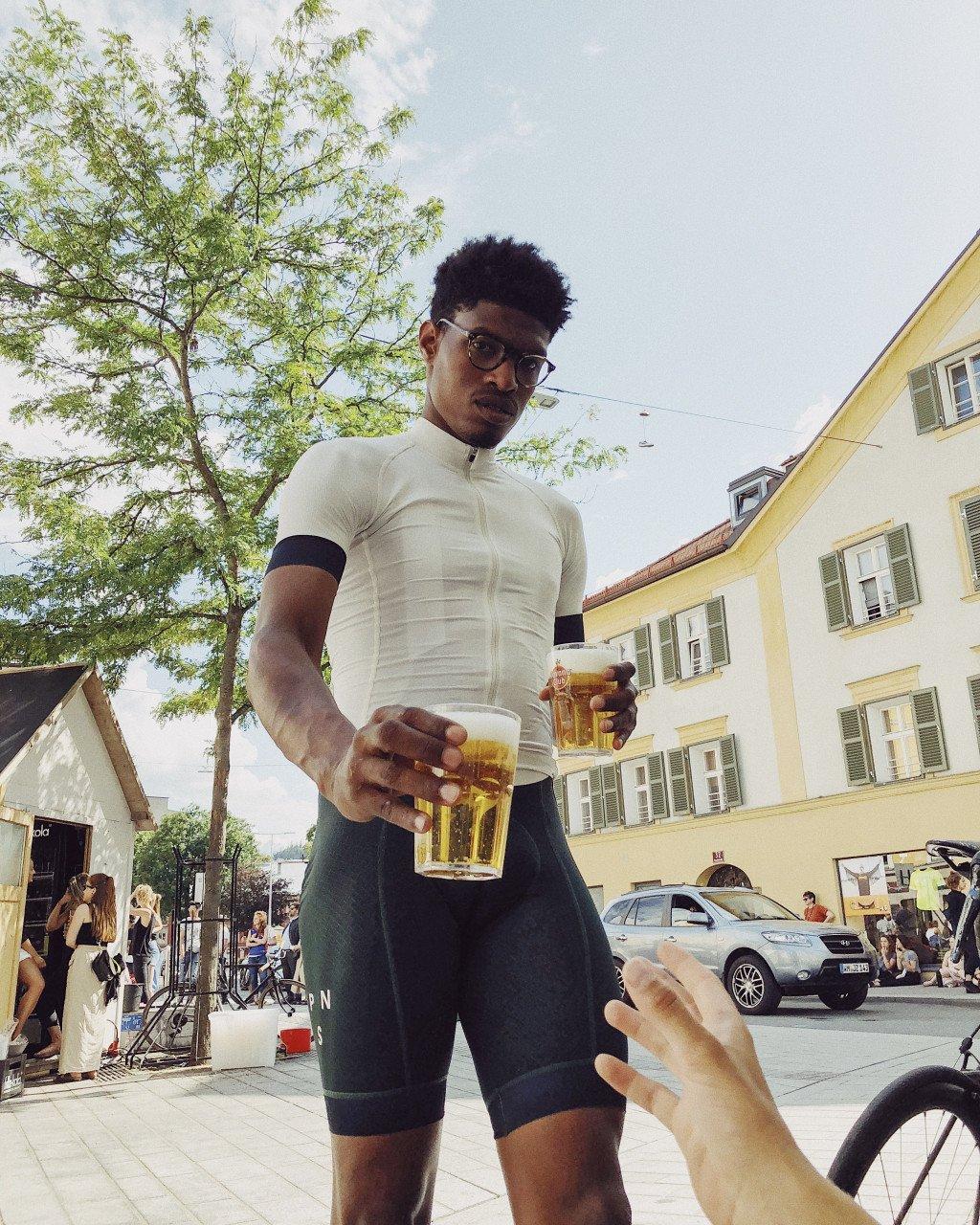 Model wearing cream jersey with black sleeve bands and black cycling shorts holding beer in town square