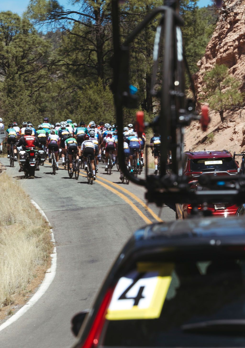 Cycling peloton racing on desert road with support vehicles during Tour of the Gila