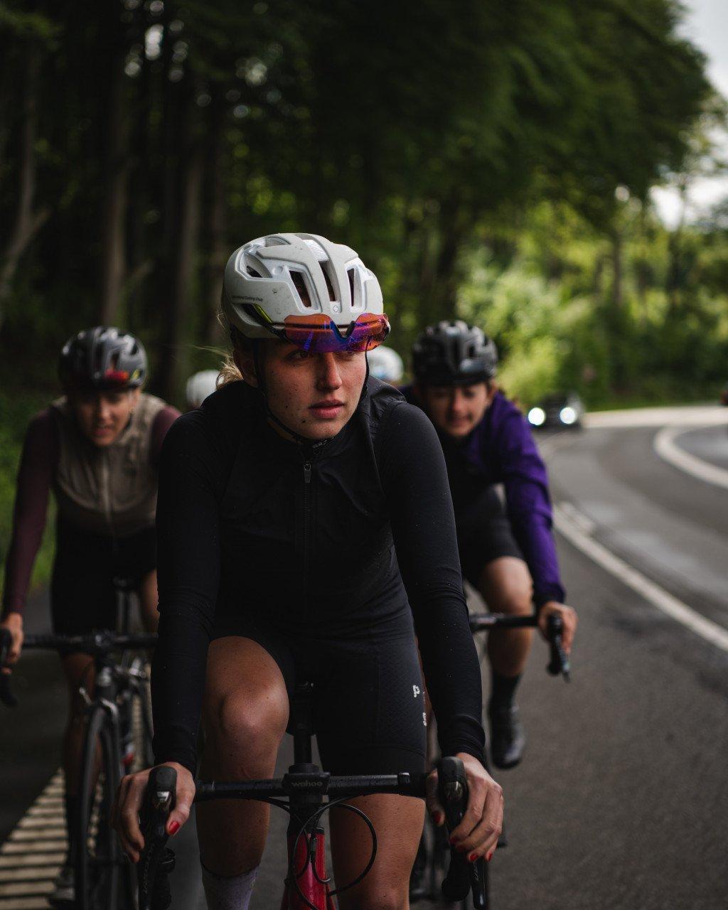 Model wearing black long sleeve cycling jersey with quarter zip cycling on road with group