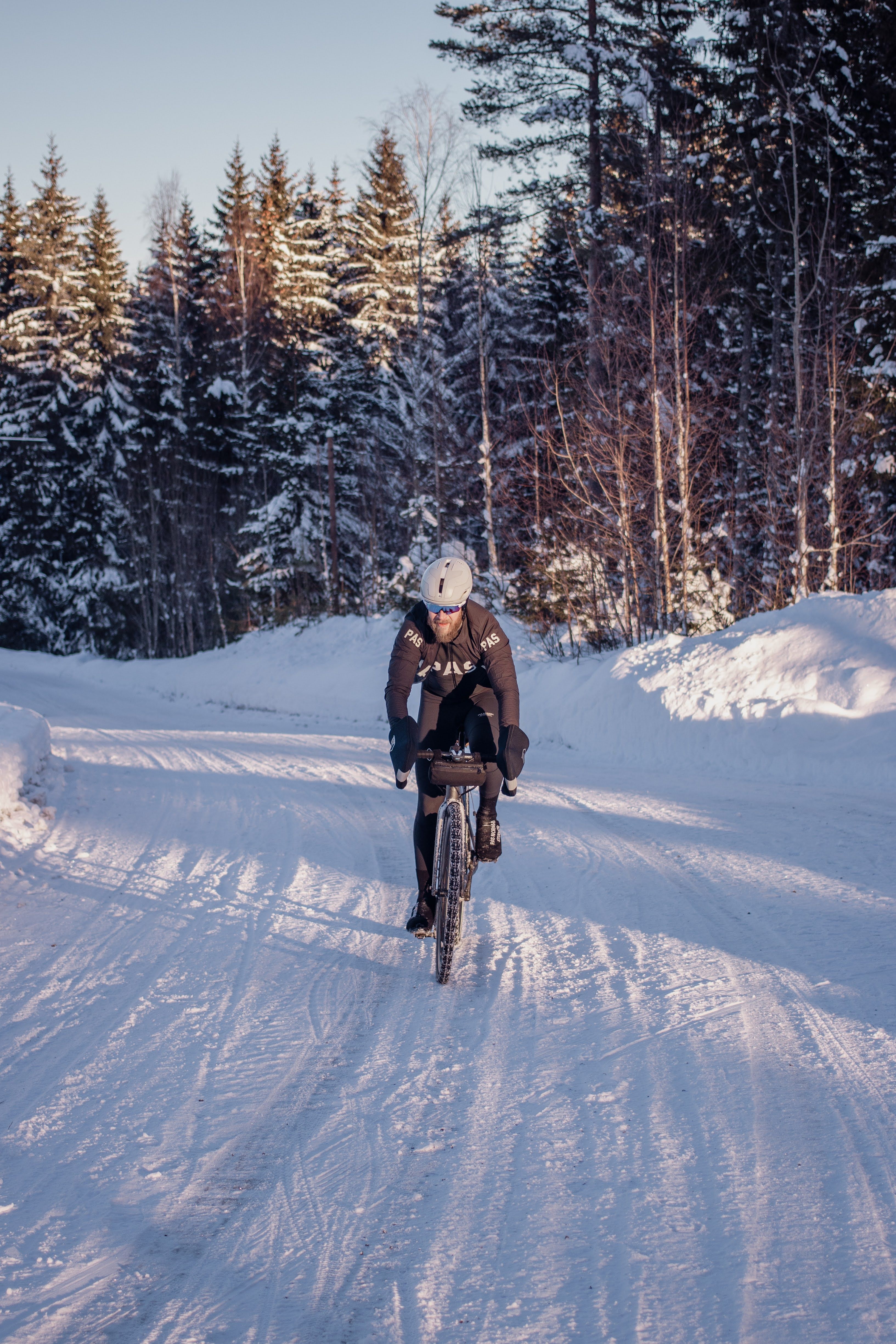 Model wearing brown cycling jersey and black tights riding on snowy forest road