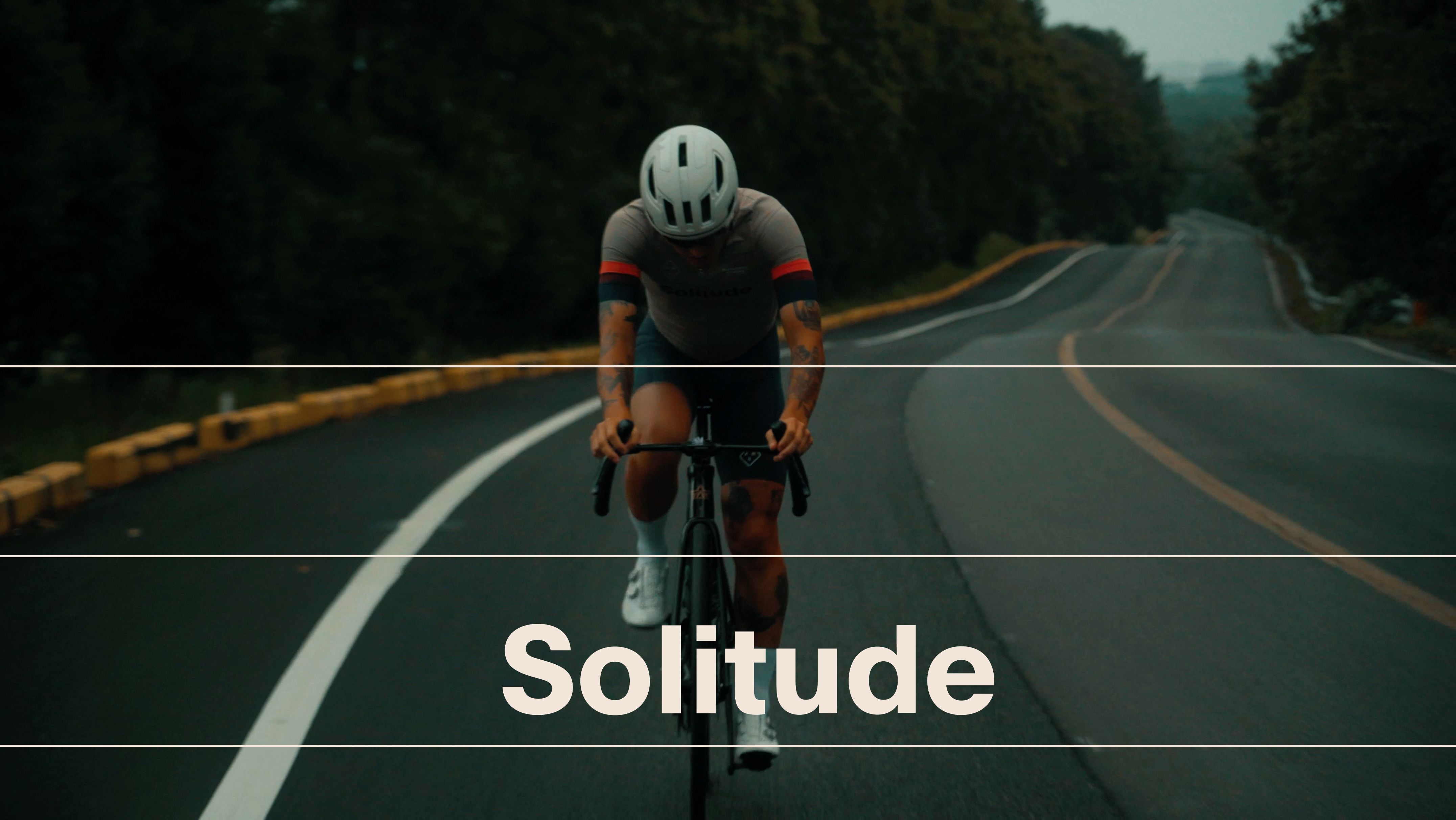 Model wearing dark grey cycling jersey with red sleeve stripes riding time trial bike on empty road