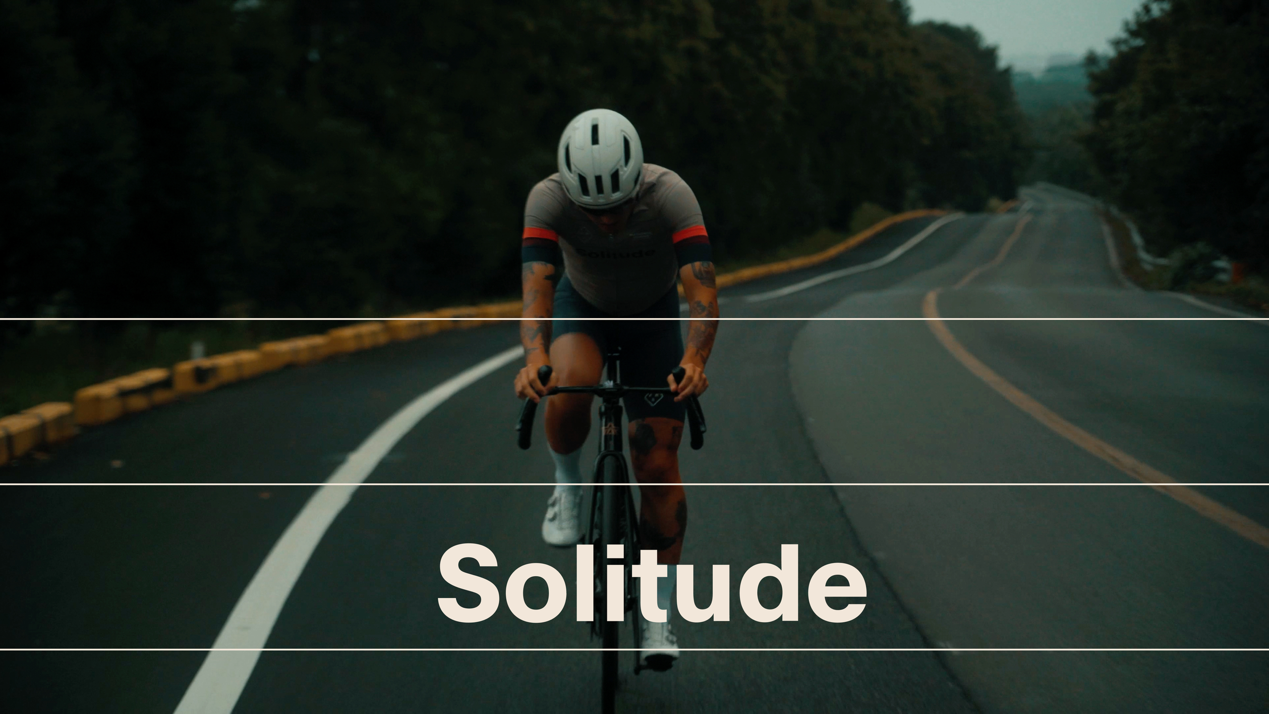 Model wearing dark grey cycling jersey with red sleeve stripes riding time trial bike on empty road