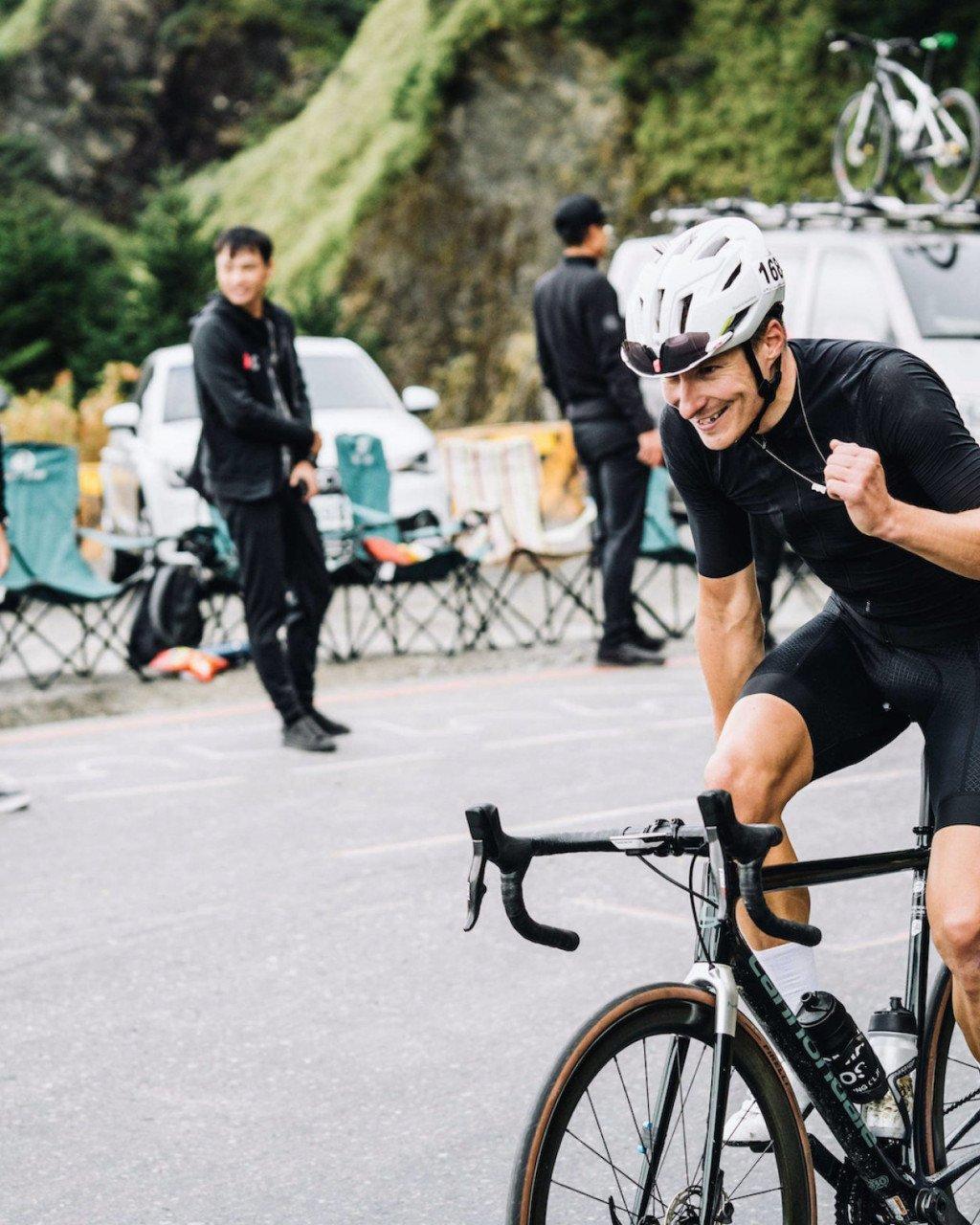 Model wearing black cycling kit with white helmet celebrating on time trial bike at race finish
