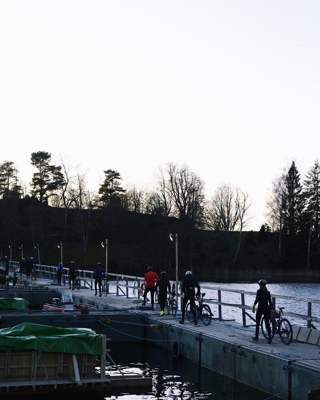 Cyclists gathered on wooden dock with bikes at waterside during winter evening