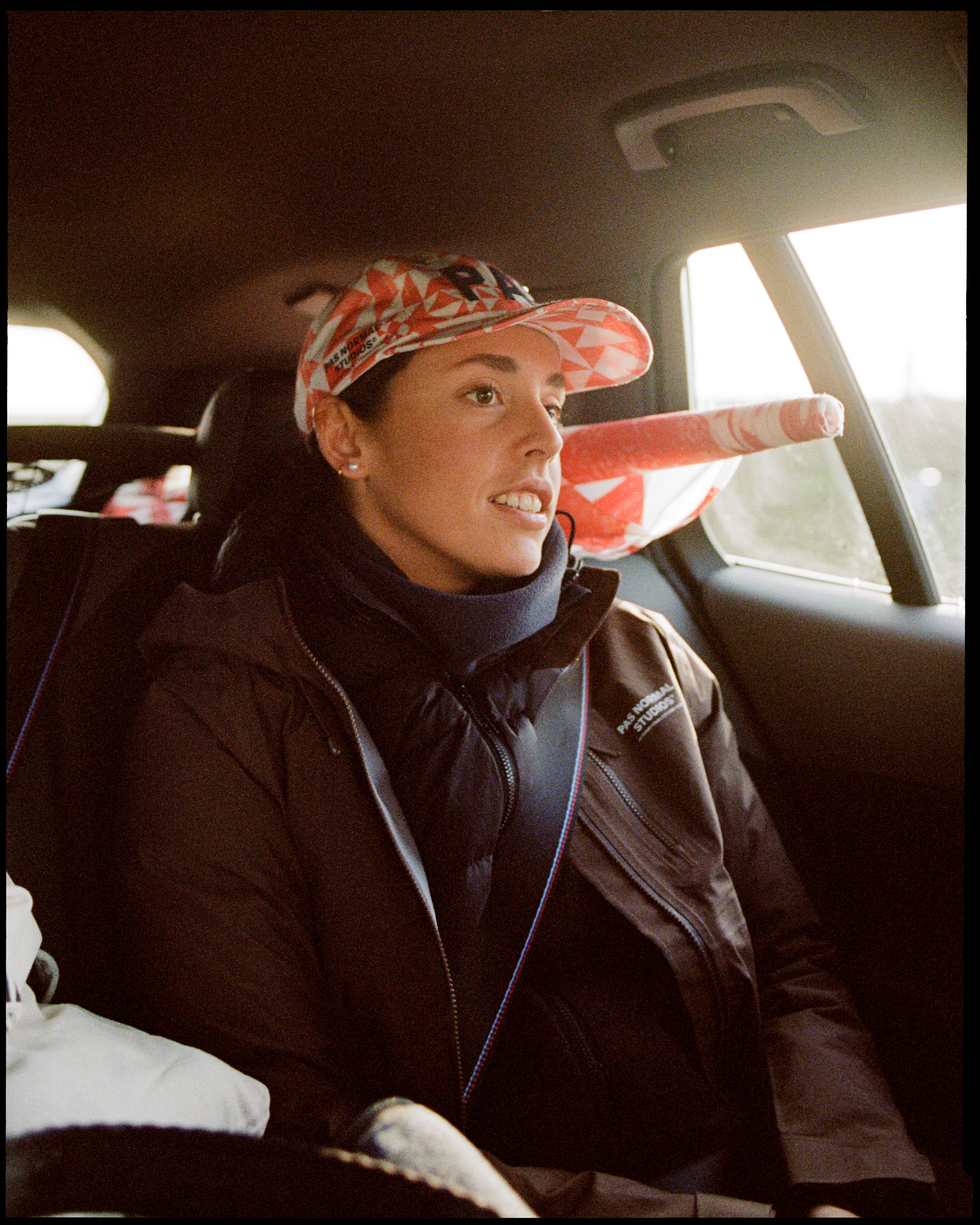 Model wearing red patterned cycling cap and dark zip jacket in car interior