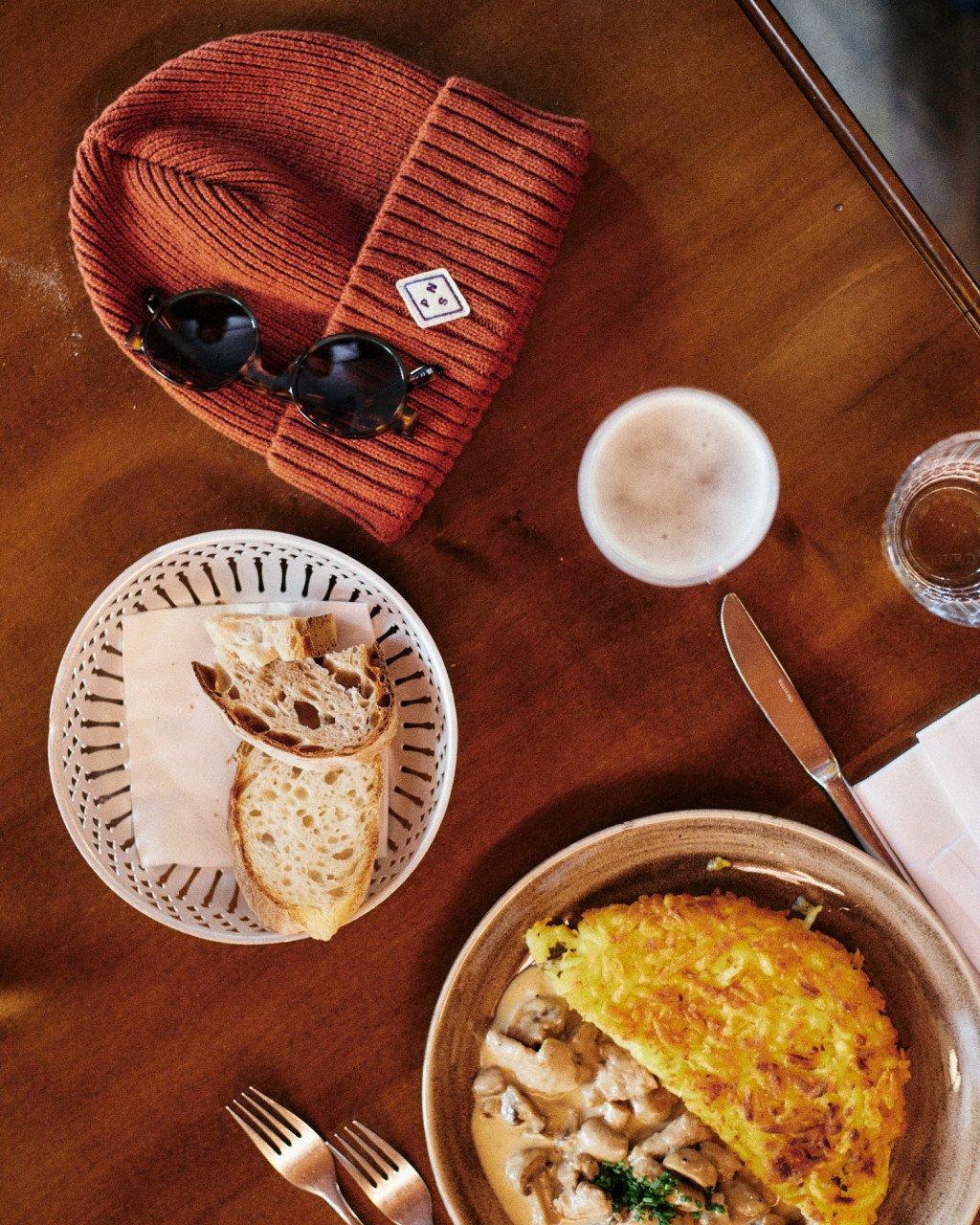 Off-Duty Beanie in orange ribbed knit with logo patch and sunglasses on wooden table