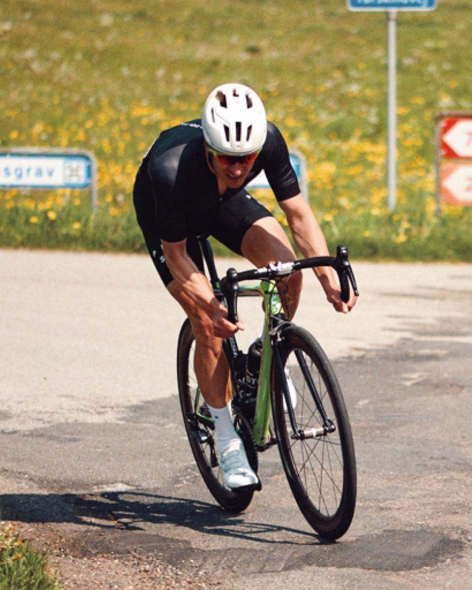 Model wearing black cycling kit in aerodynamic time trial position on road bike during race