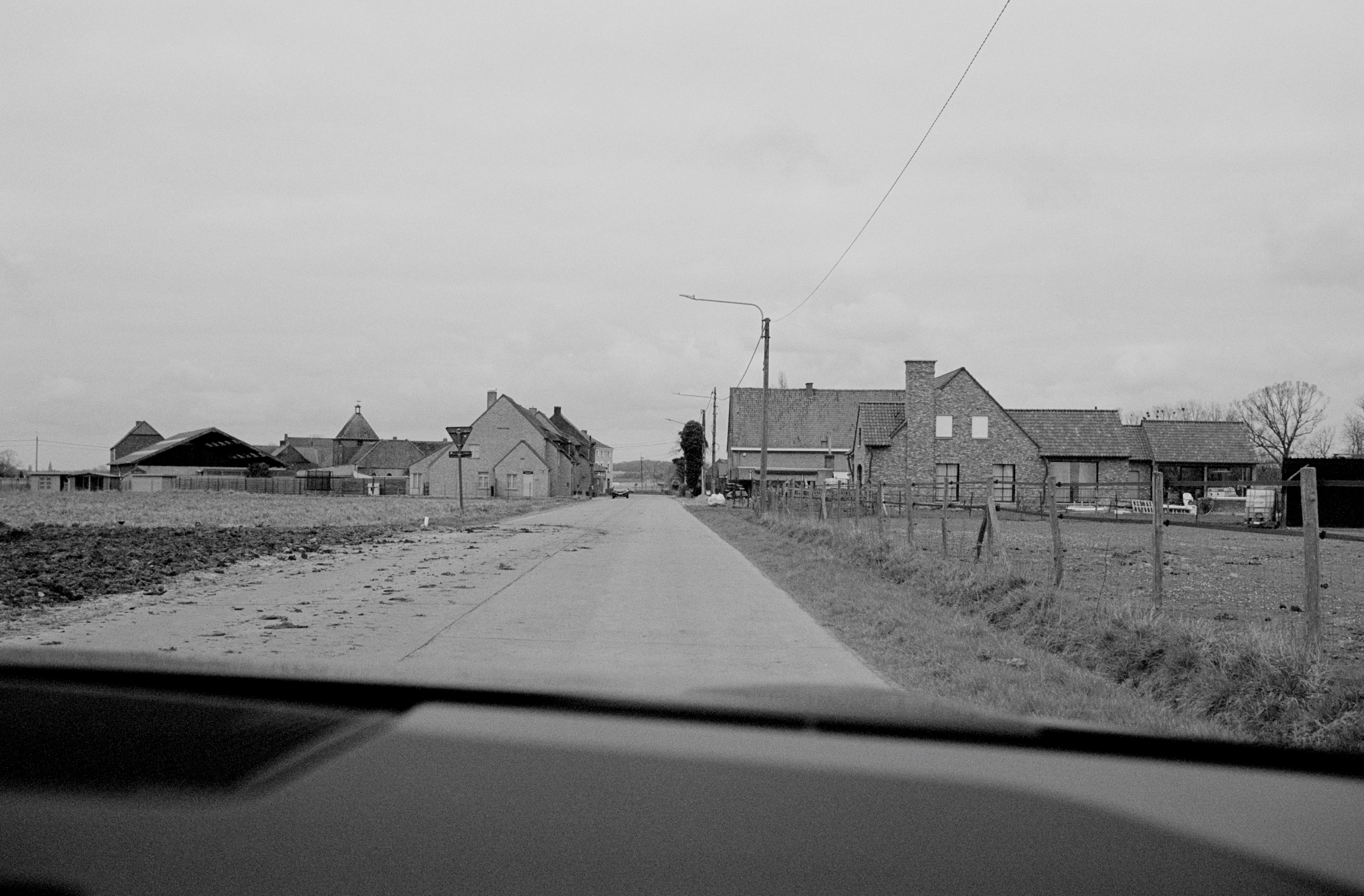 View from car dashboard of rural road through small village with brick houses and farmland