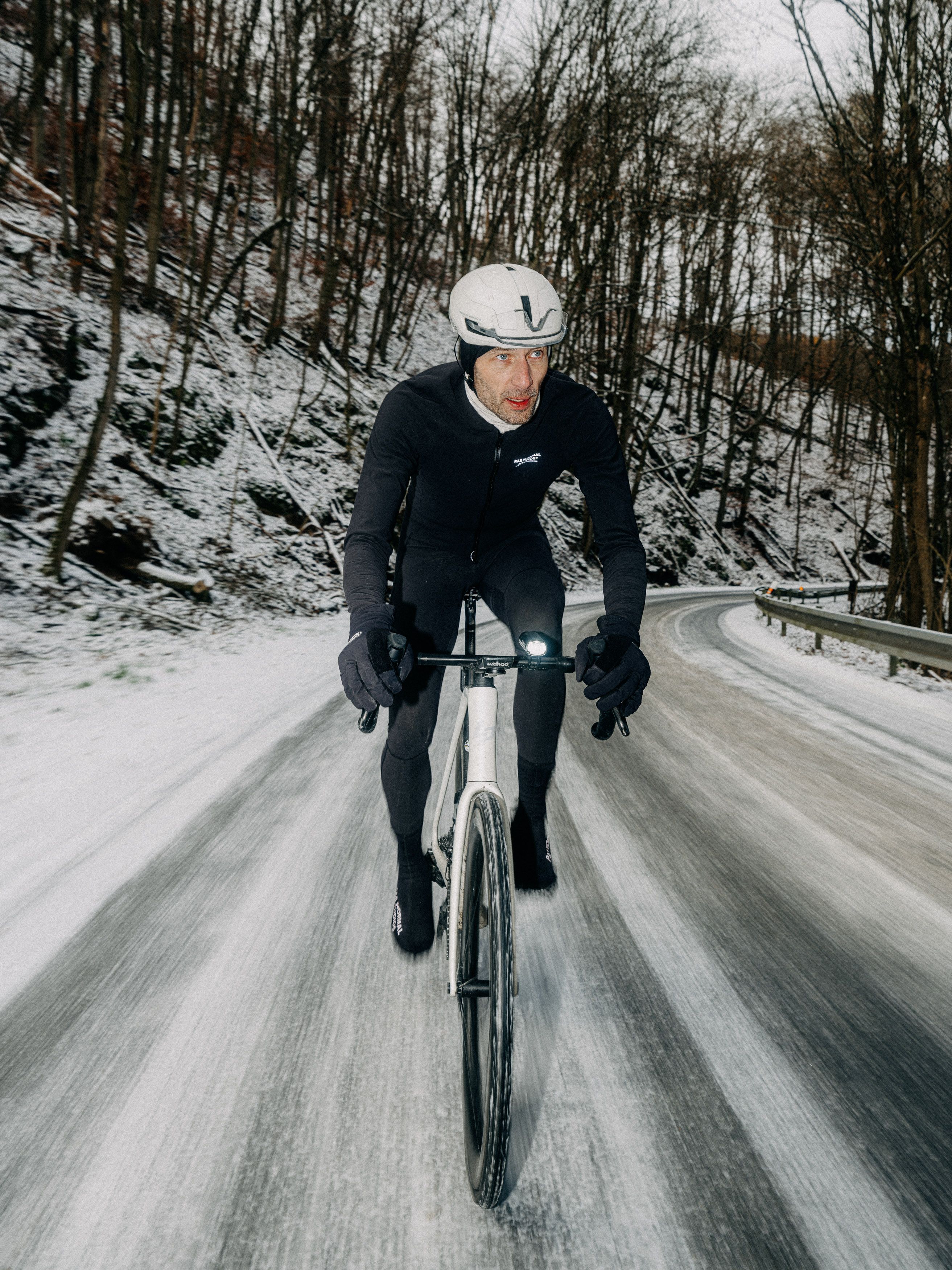 Model wearing black cycling kit on time trial bike on snowy winter road