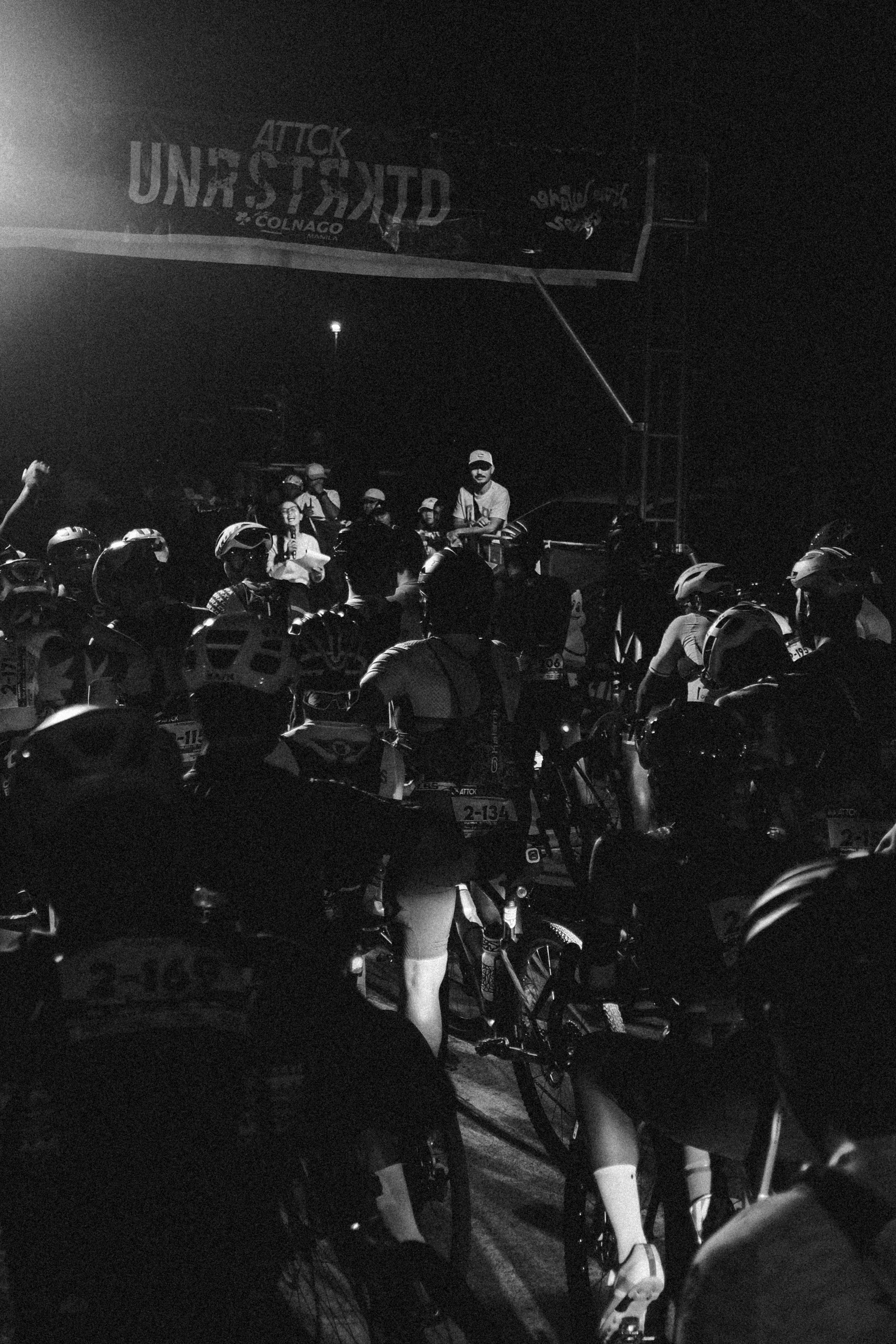 Cyclists gathered at night race start line in Philippines with helmets and race numbers