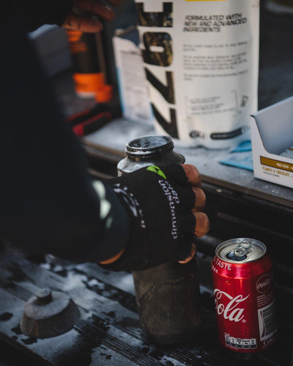Hand holding black drink bottle with green logo amid cycling nutrition products