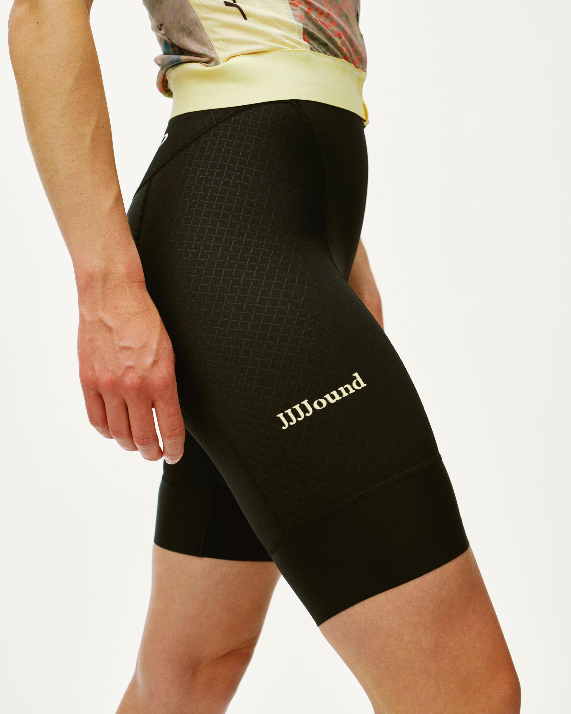 Black JJJJound Mechanism bibs on model, side view with textured panel and white leg branding