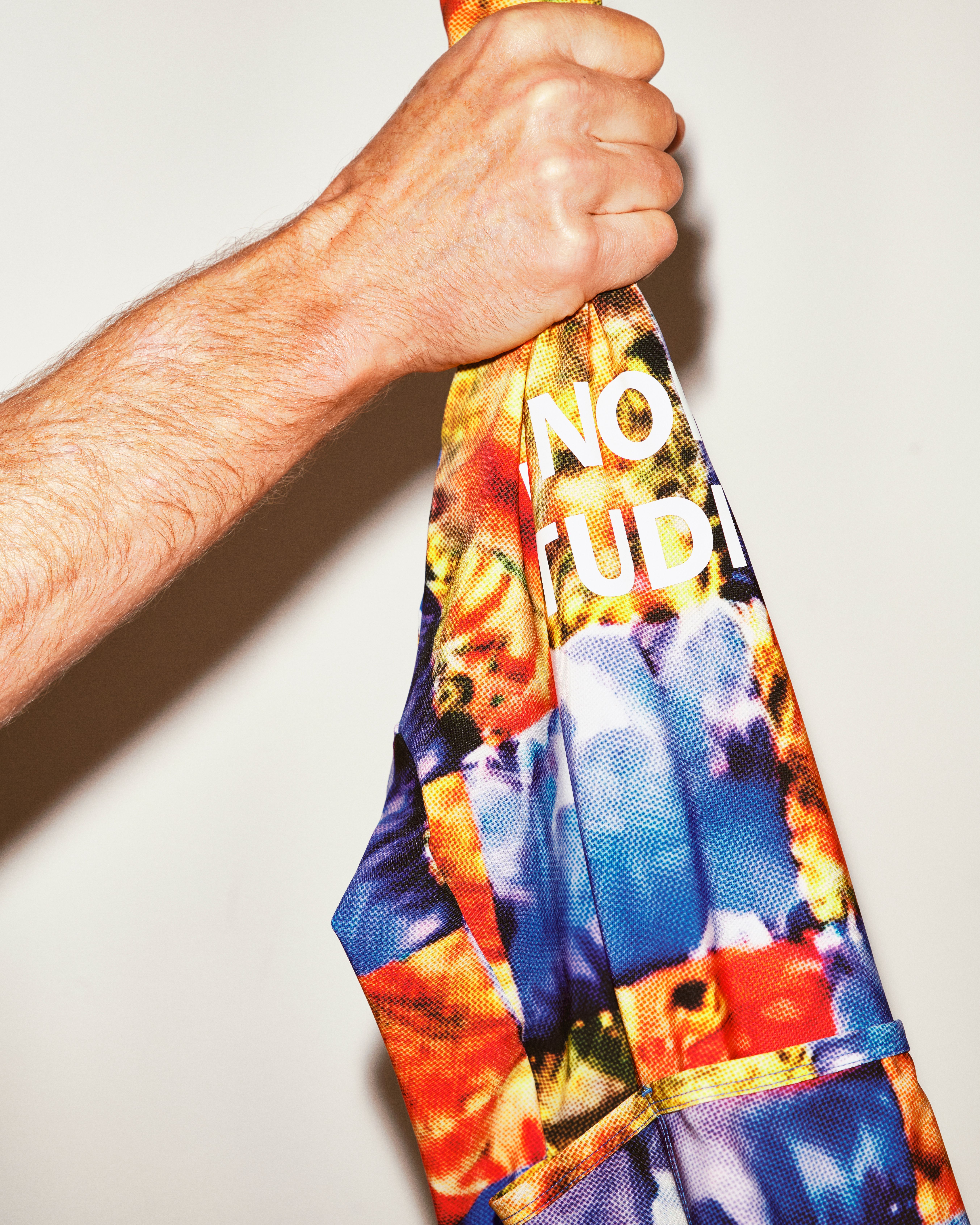 Hand holding Essential arm warmers with multicolored digital print pattern and white text