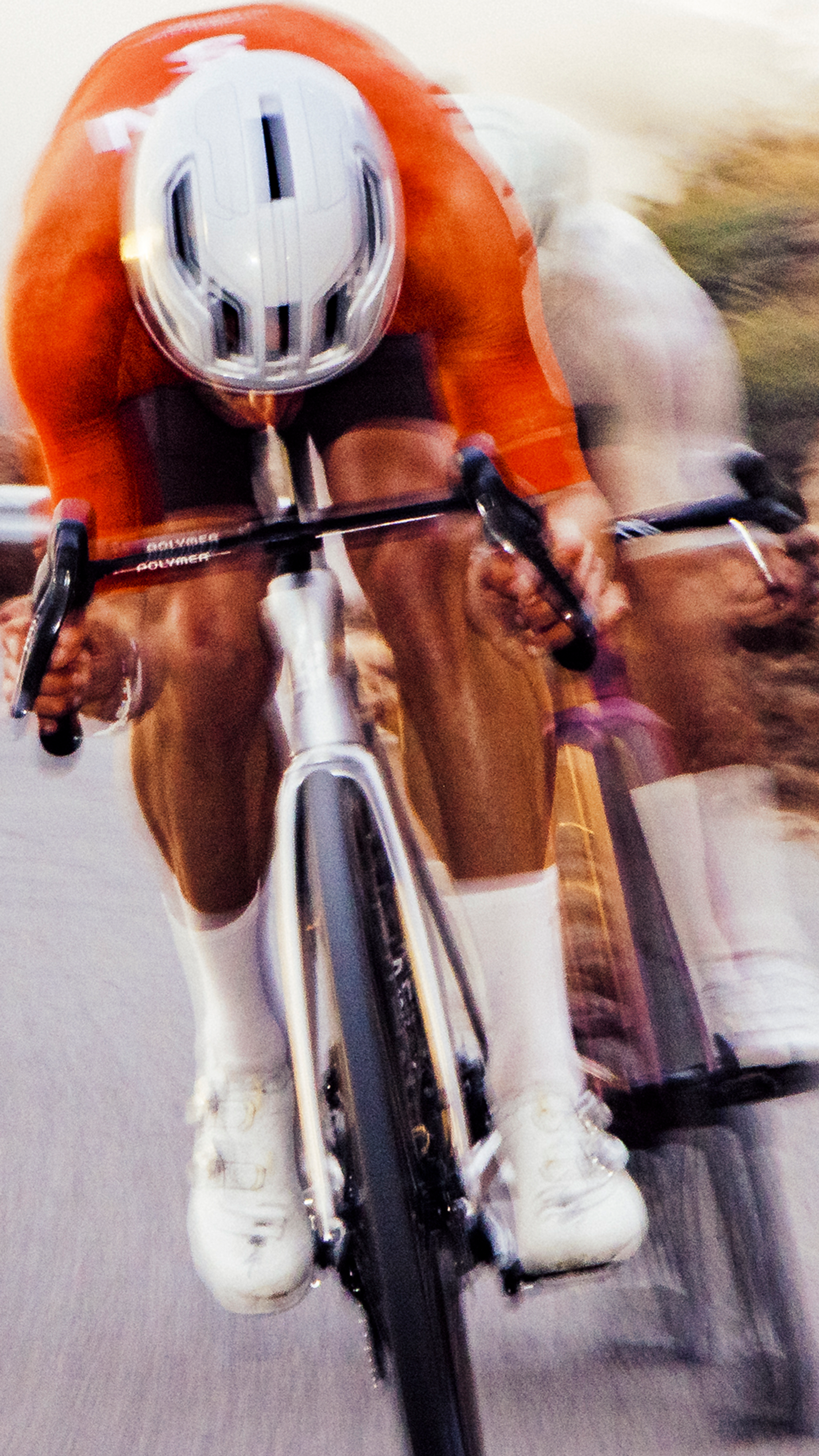 Cyclist in orange aerodynamic suit and helmet on time trial bike in motion