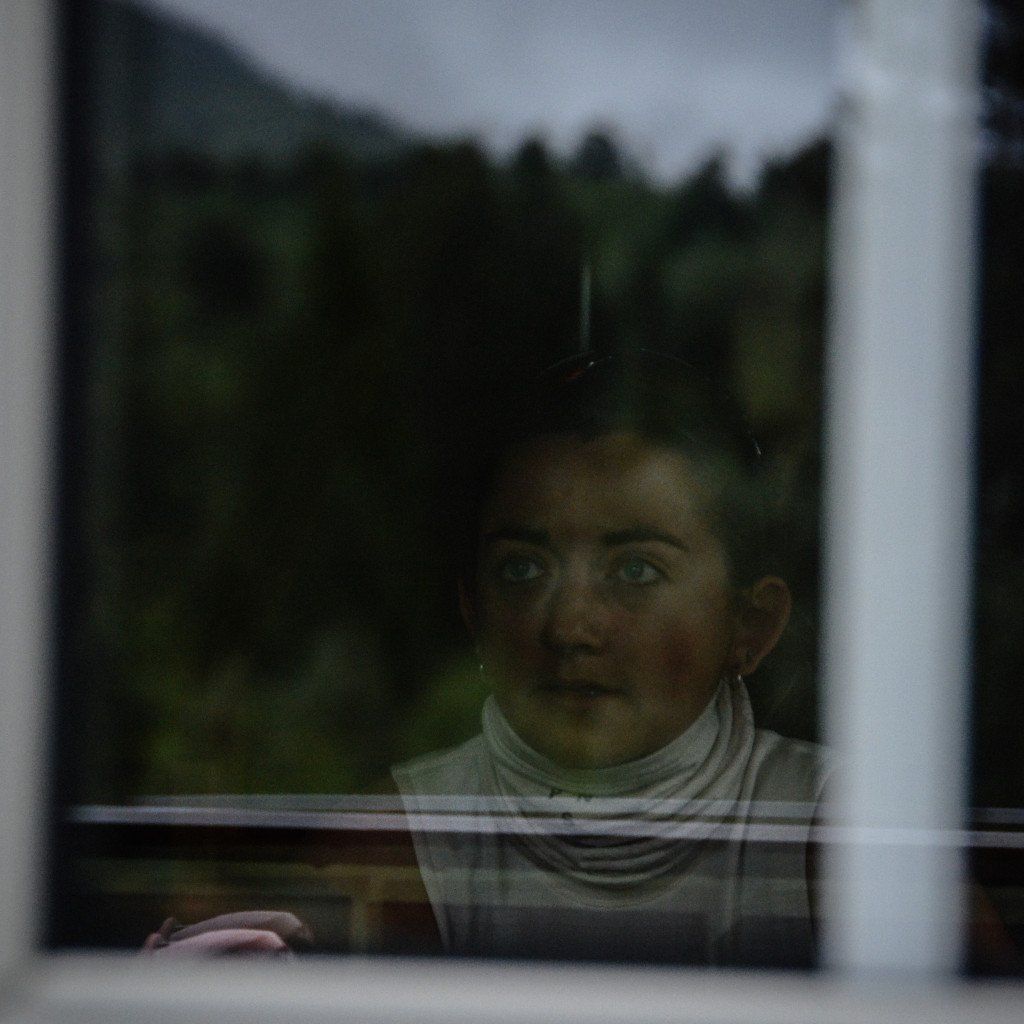 Model wearing white base layer reflected in window with green landscape background
