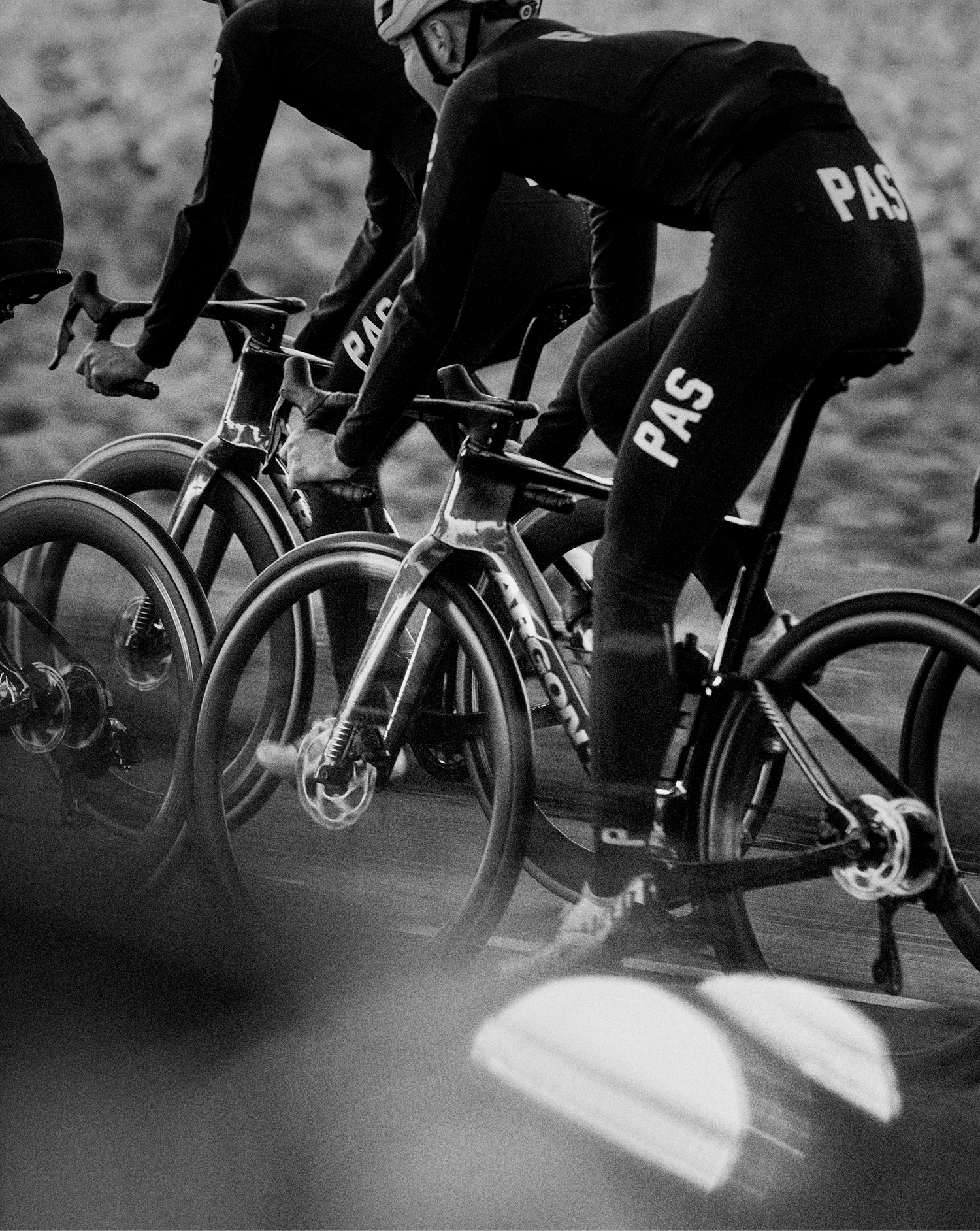 Cyclists in black apparel with collection branding during time trial race, black and white photography
