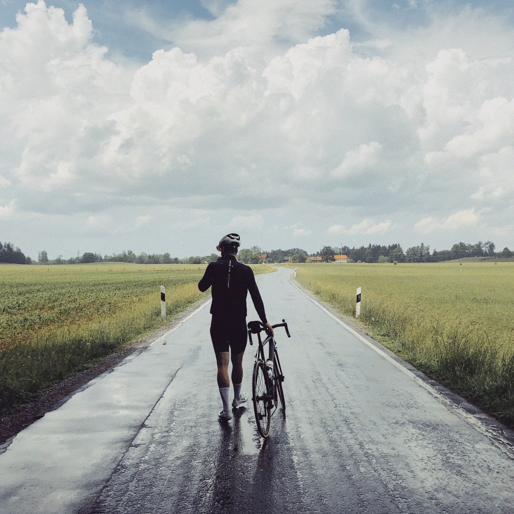 Cyclist walking with bike on empty countryside road under cloudy sky