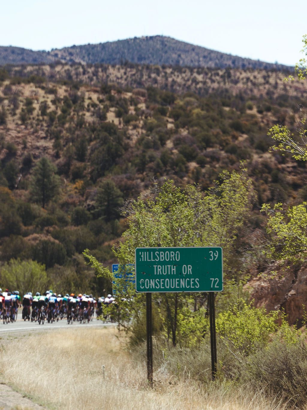 Cycling peloton racing past desert highway sign with hills in background