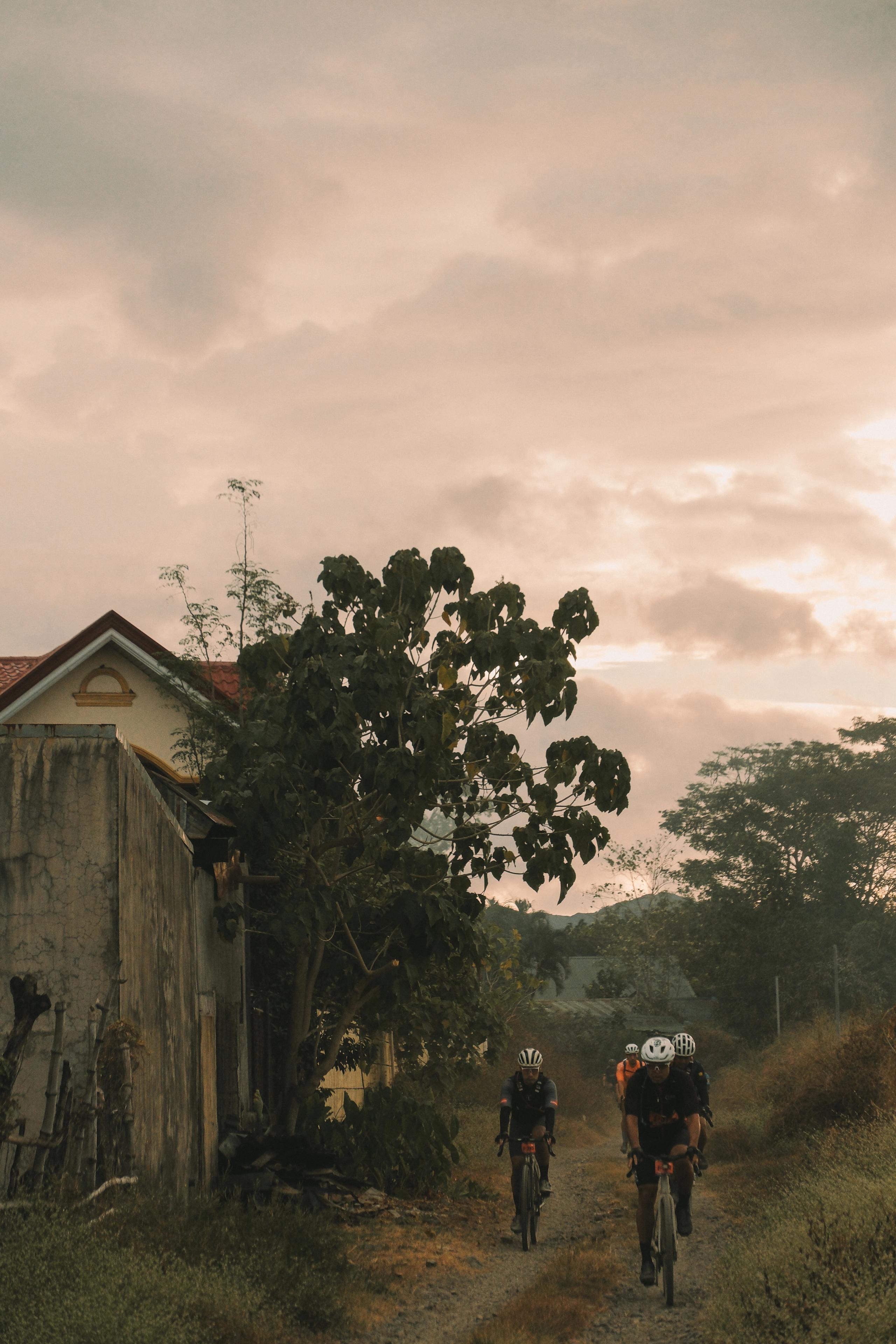 Two cyclists riding gravel bikes through rural Philippines village at sunset