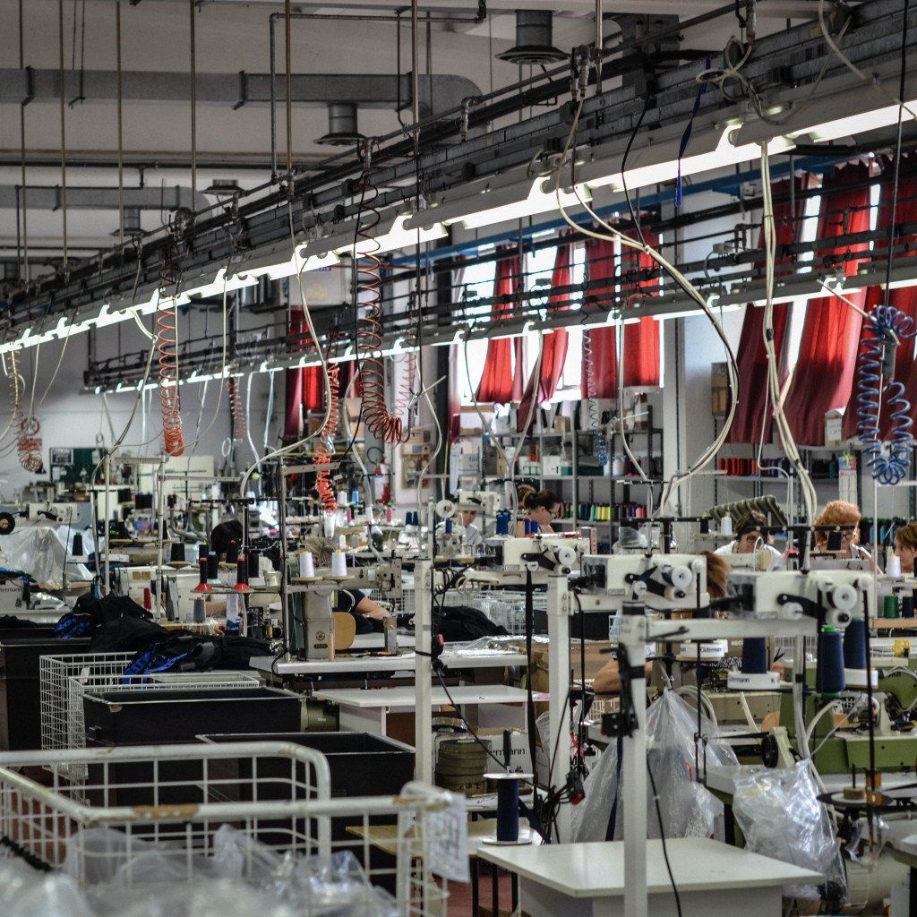 Garment manufacturing facility with sewing machines, workers, and red fabric hanging from overhead systems