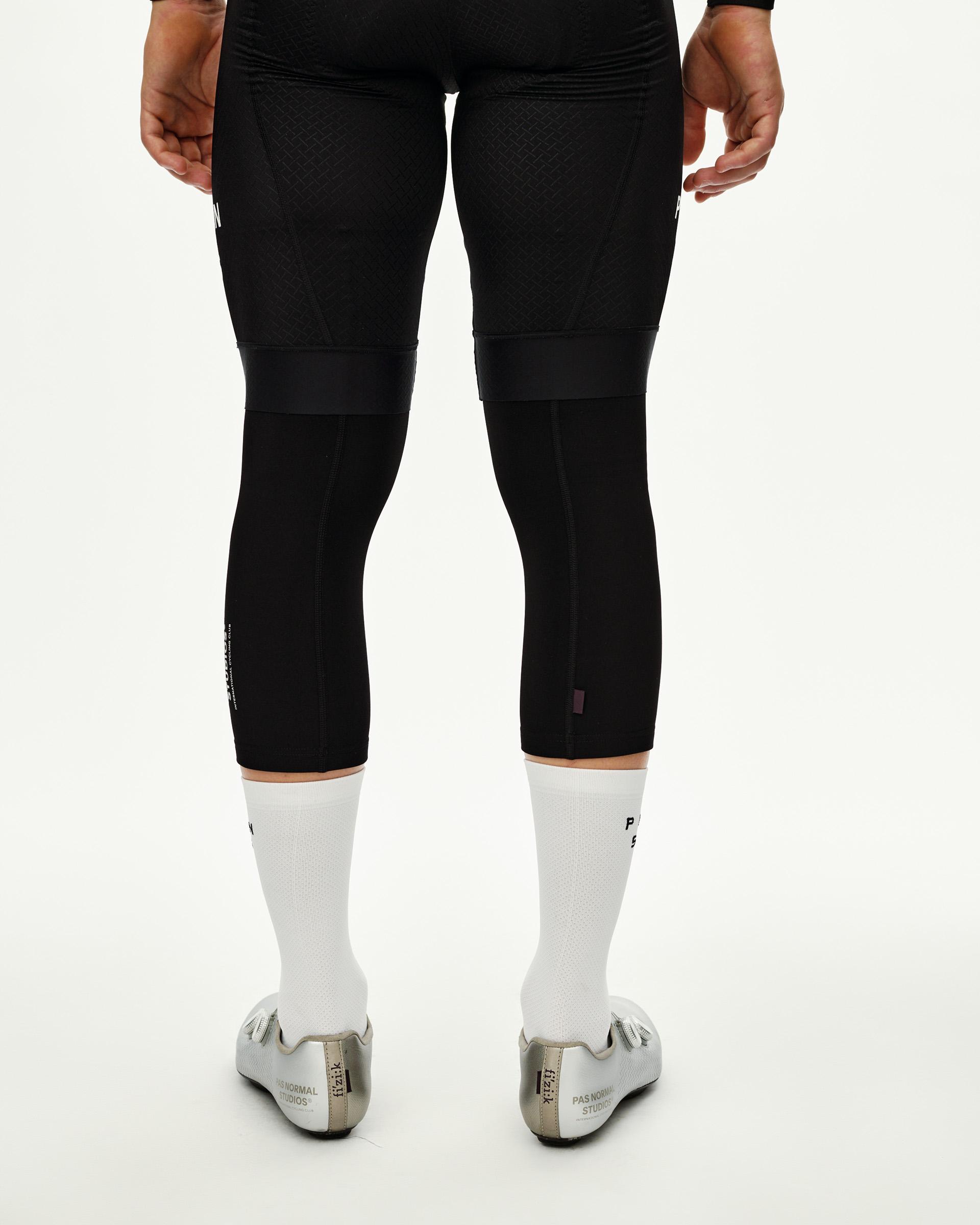 Black cycling knee warmers, rear view on model with elastic upper band and small purple tab detail
