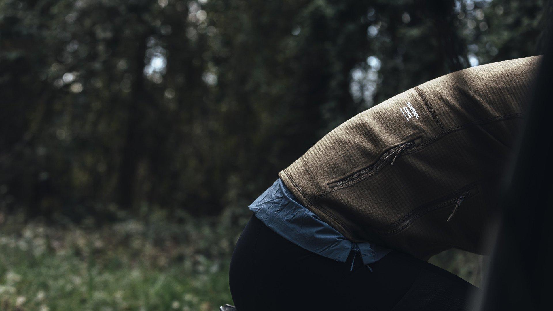 Model wearing brown ribbed long sleeve jersey with blue shorts in outdoor forest setting