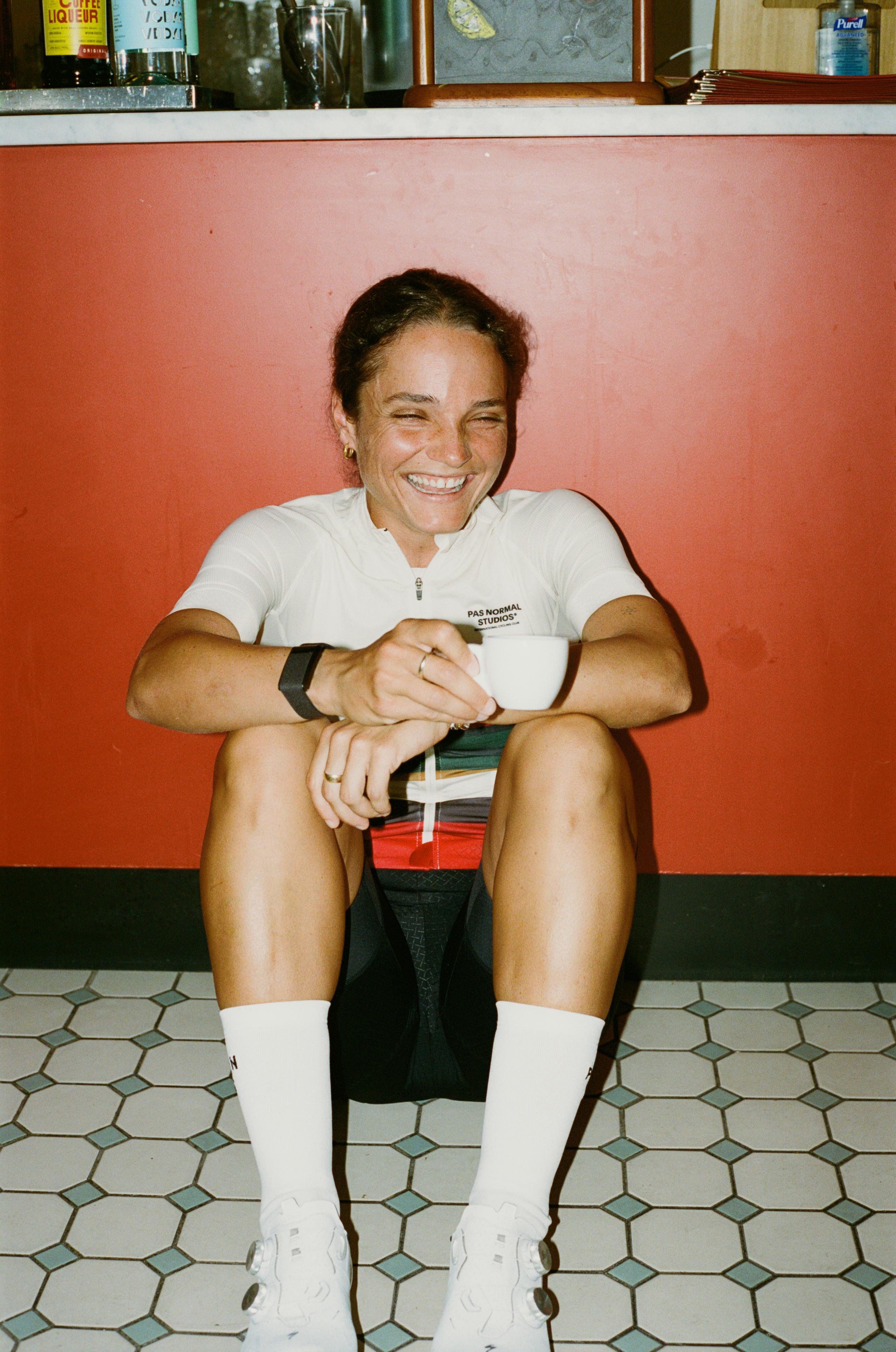 Model wearing white Mechanism jersey with logo, black shorts and white socks, sitting in casual pose