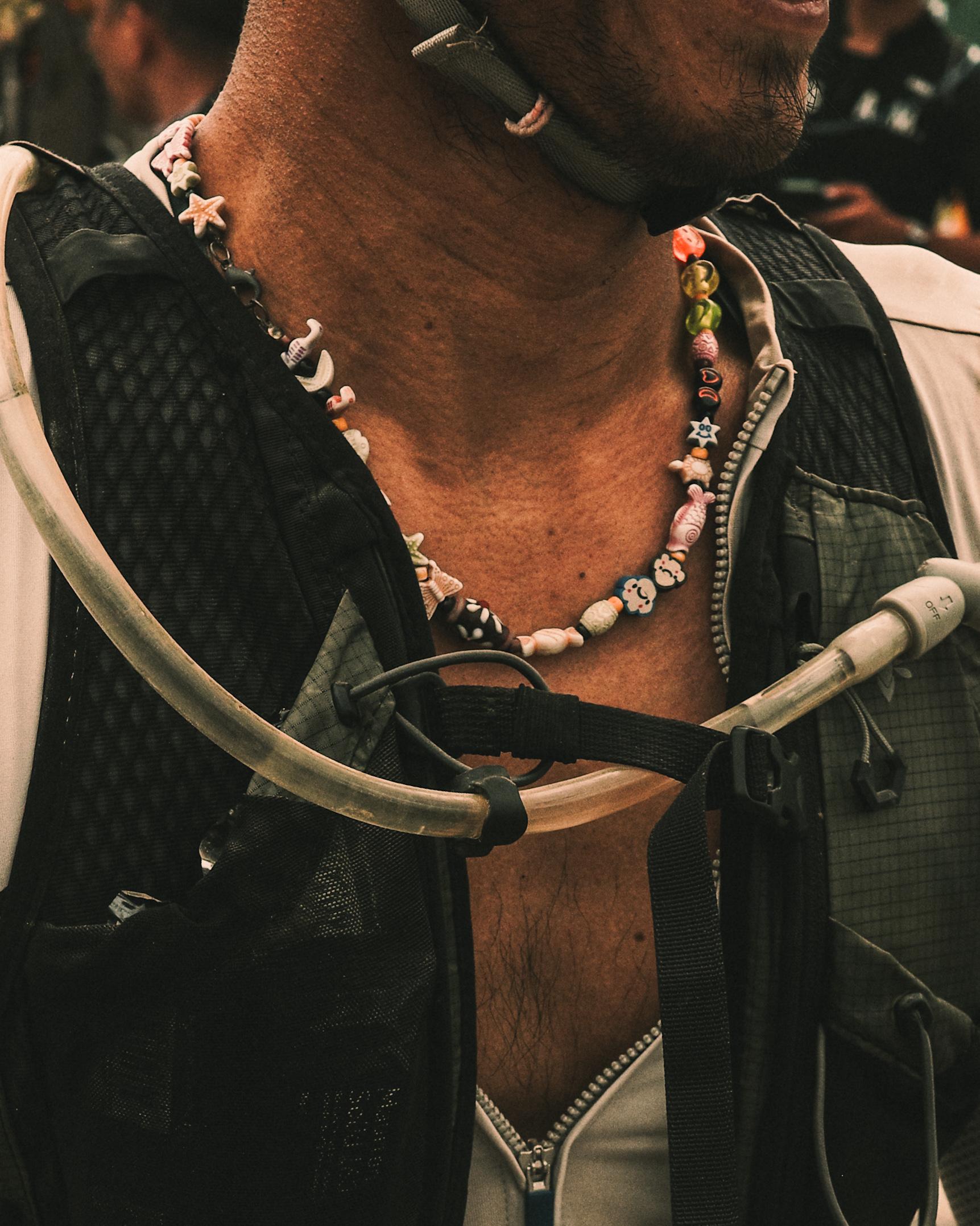 Model wearing black cycling jersey with colorful beaded necklace, holding bike handlebars