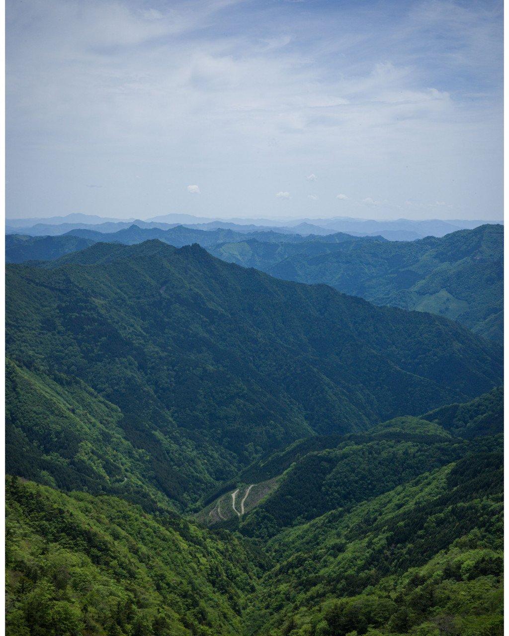 Rolling green mountains and valleys with winding road visible in distance under cloudy sky