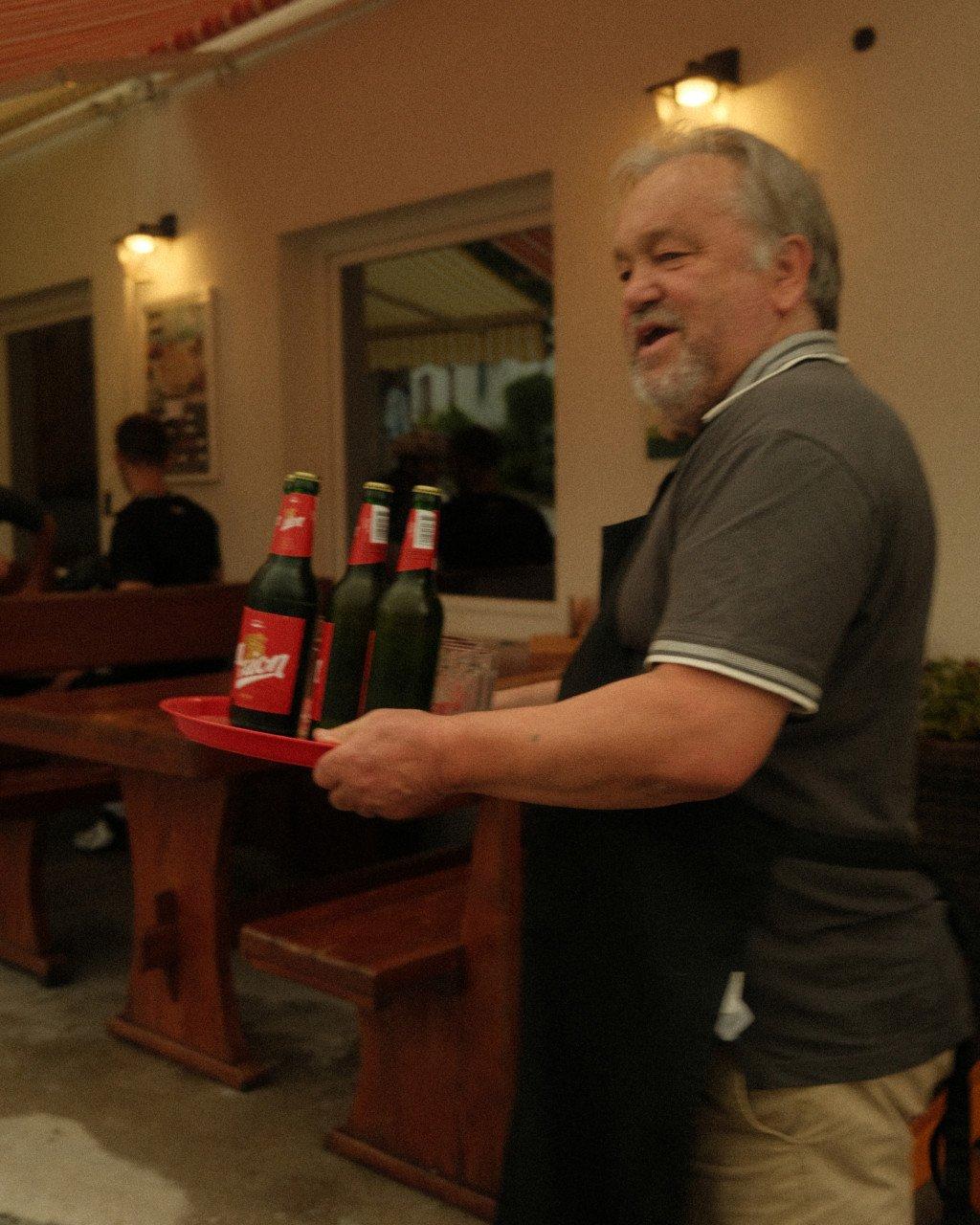Man carrying beer bottles on red tray in restaurant setting