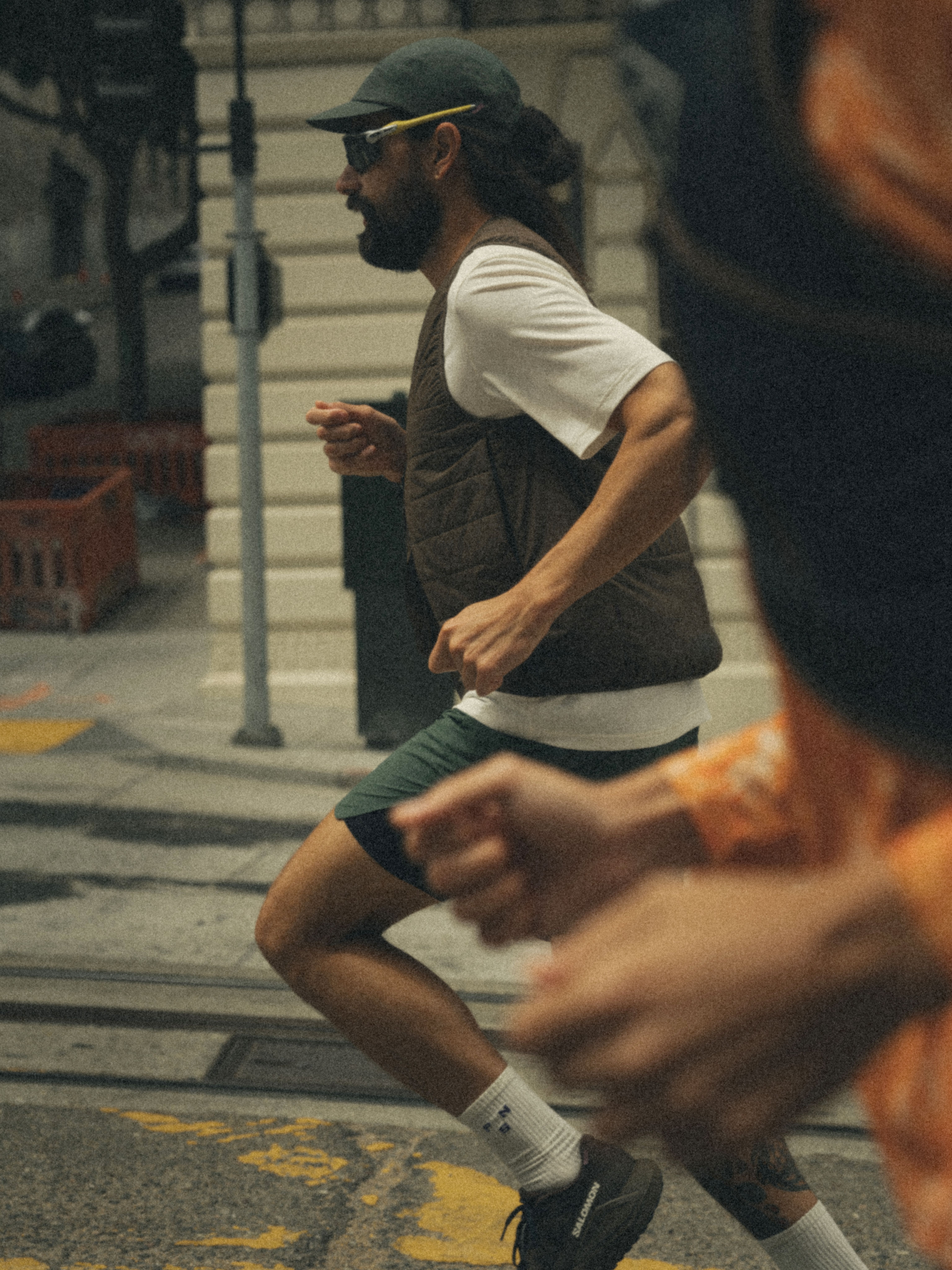 Model wearing white t-shirt and olive vest running on city street