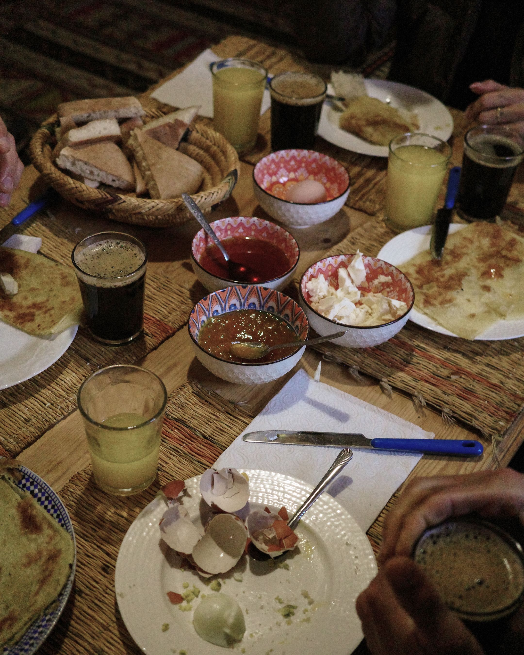 I notice this image shows a meal spread with traditional food and drinks, but it doesn't appear to contain any Pas Normal Studios cycling apparel or products. Since this is meant for alt text on the Pas Normal Studios website for a story about "Sahara Gravel - Nils Correvon," I would describe what's actually visible in the image:

Traditional meal spread with flatbread, various bowls of food, and drinks on woven placemat