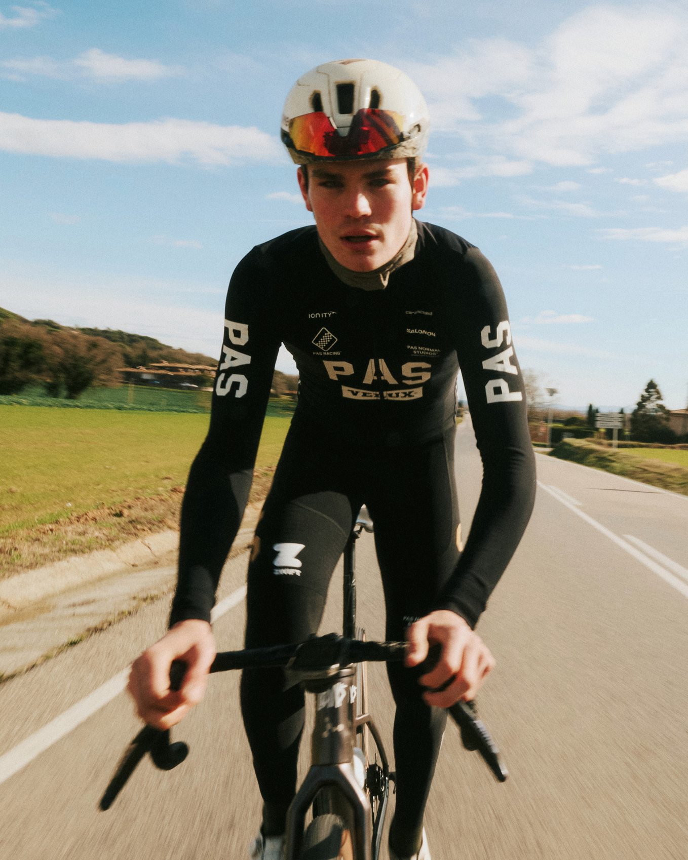 Model wearing black PAS racing skinsuit with white logo on time trial bike on country road