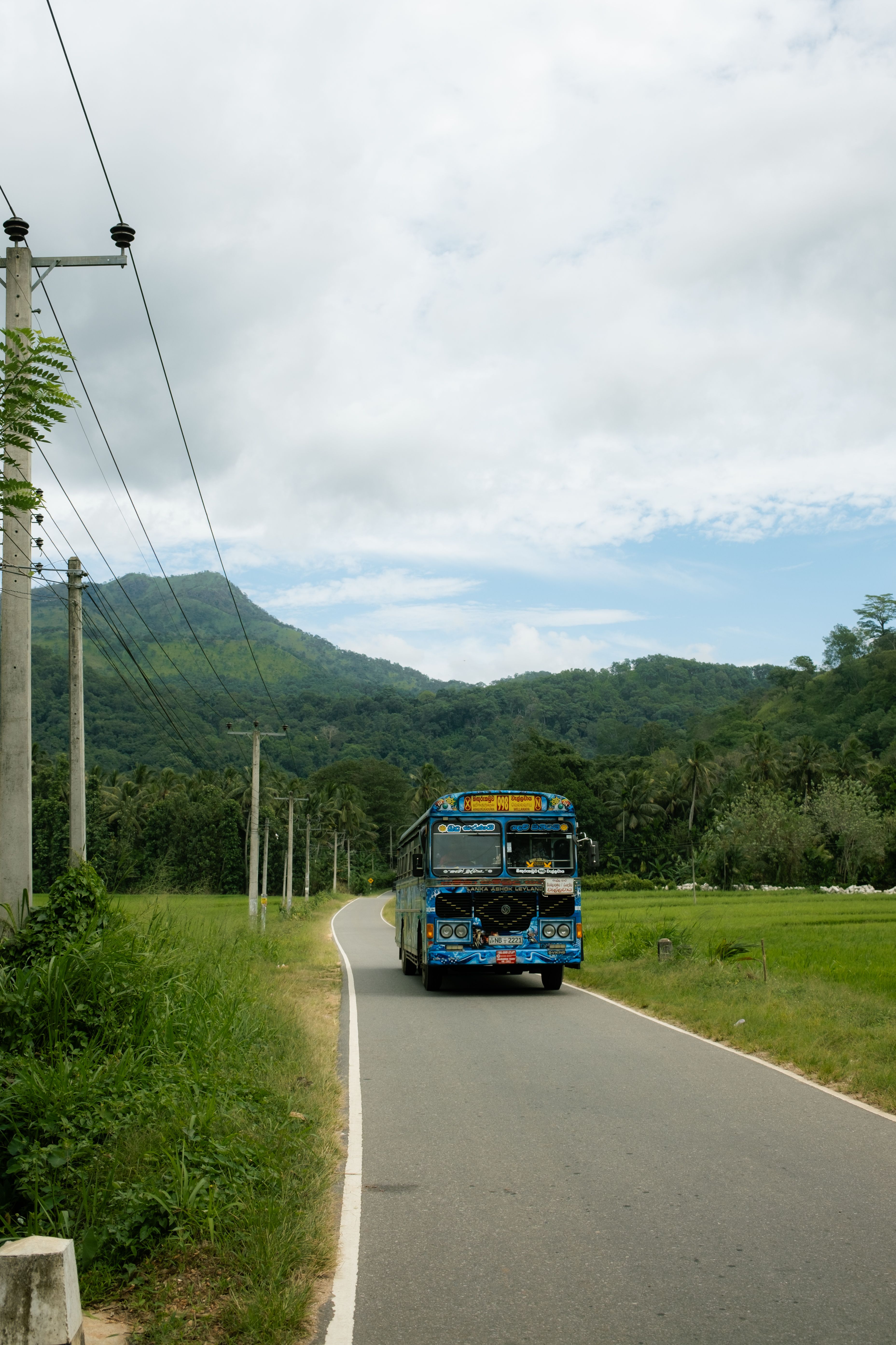 Blue bus on rural road with mountains and green fields in background