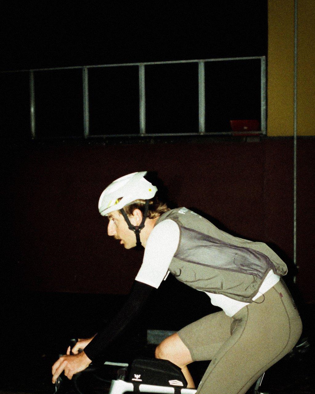 Model wearing white cycling jersey and olive green vest with white aerodynamic helmet in cycling position