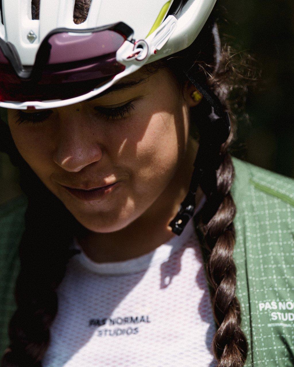 Model wearing white cycling helmet with green jersey, eyes closed in sunlight