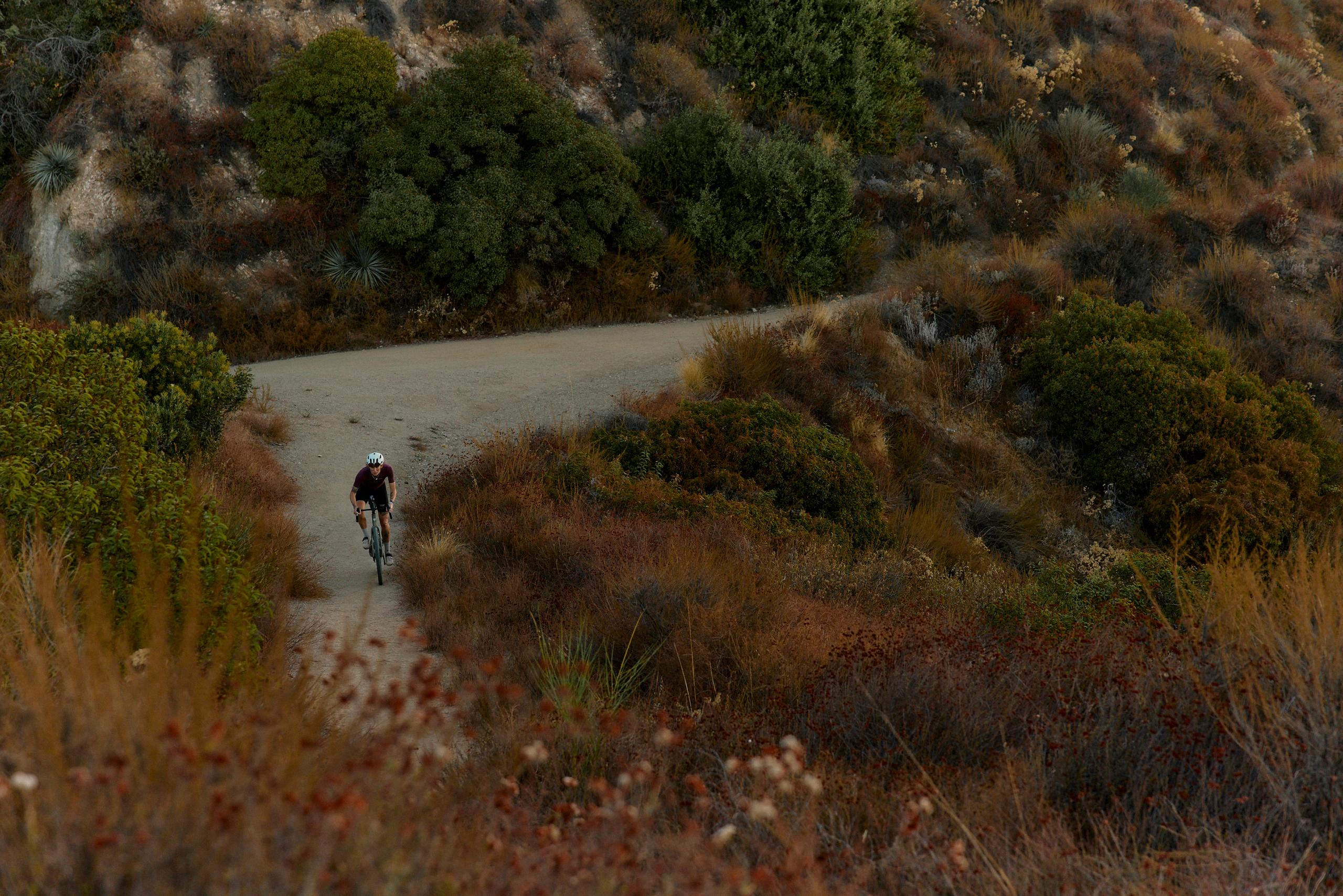 Cyclist riding through winding dirt road surrounded by autumn vegetation and hills