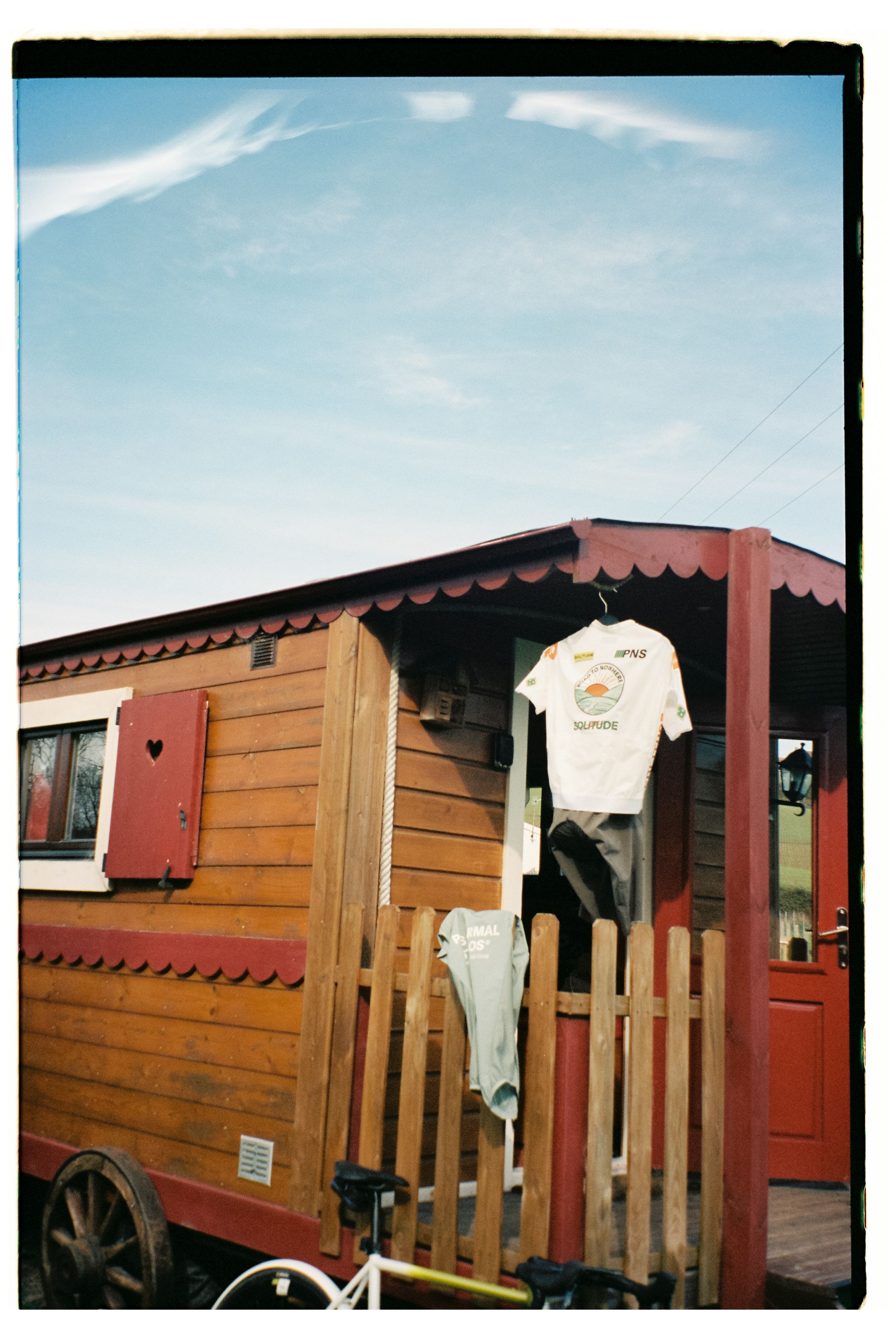 White cycling jersey and black shorts hanging on wooden cabin porch with mountain backdrop