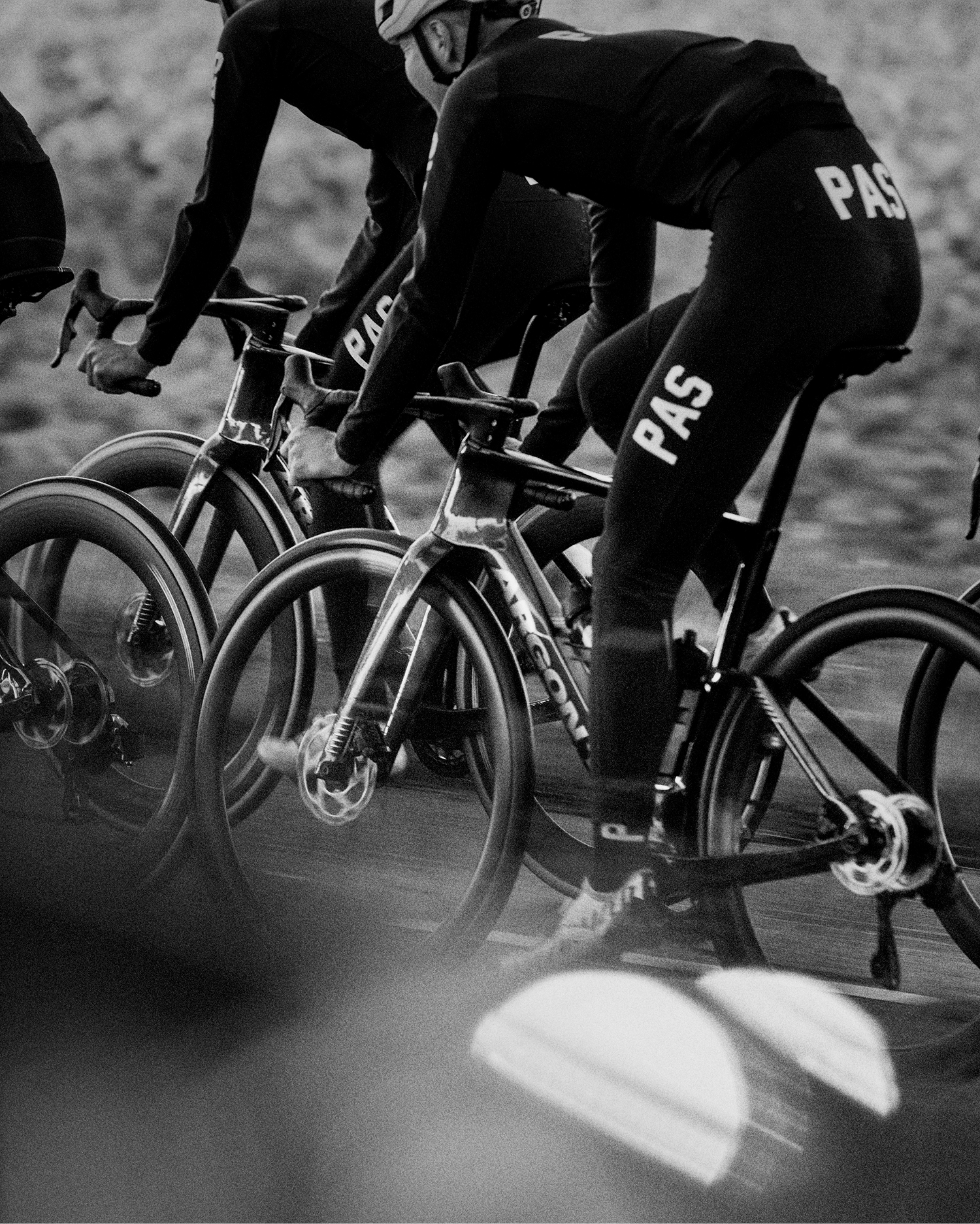 Models wearing black cycling apparel with logo lettering during time trial race in black and white