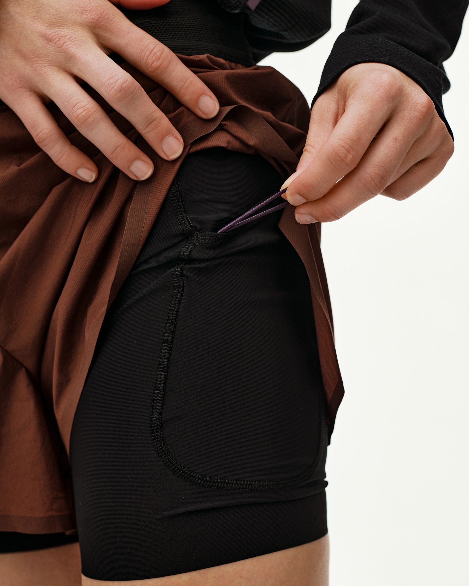 Maroon Brown Balance 2-in-1 shorts, detail view on model showing lifted outer layer and inner liner pocket
