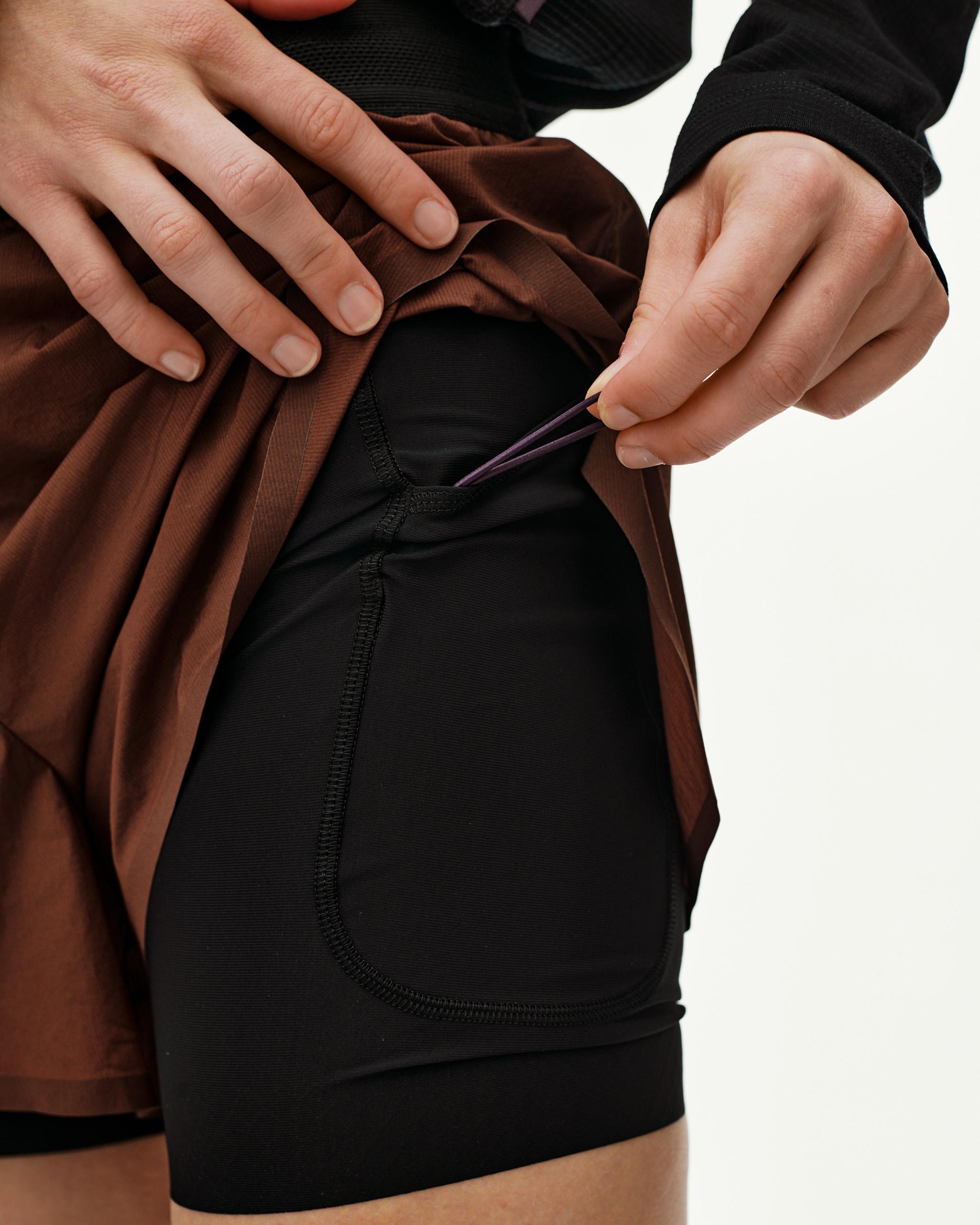 Maroon Brown Balance 2-in-1 shorts, detail view on model showing lifted outer layer and inner liner pocket