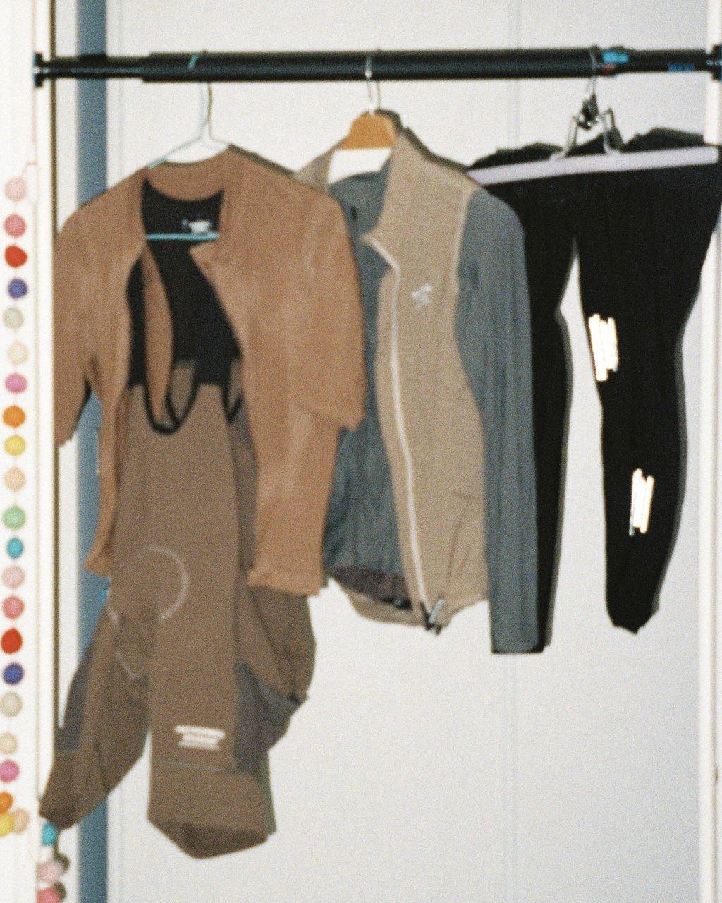 Cycling apparel hanging on rail including brown jersey, blue jacket, and black shorts