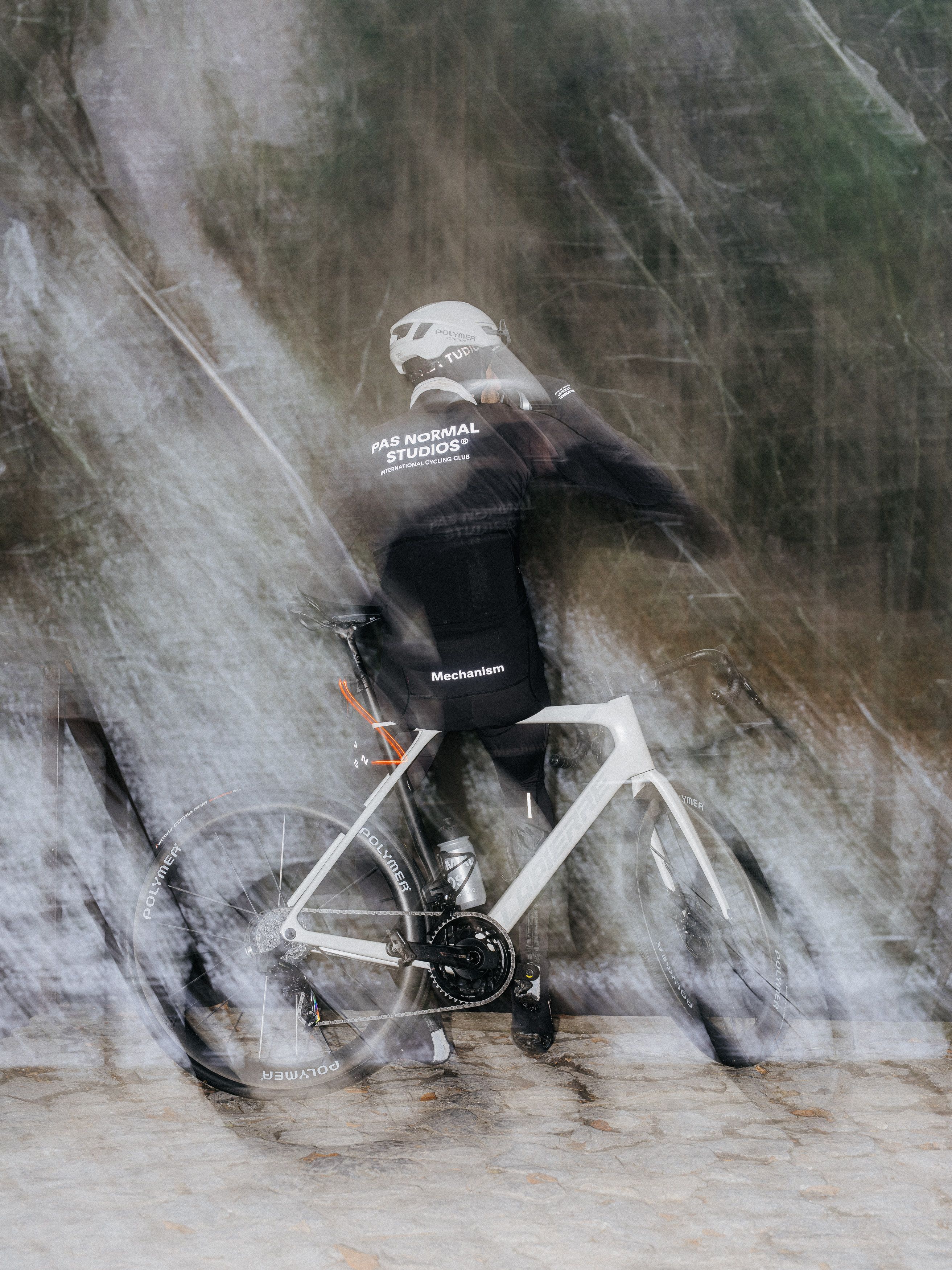 Cyclist wearing black Mechanism jersey and shorts on time trial bike in motion blur